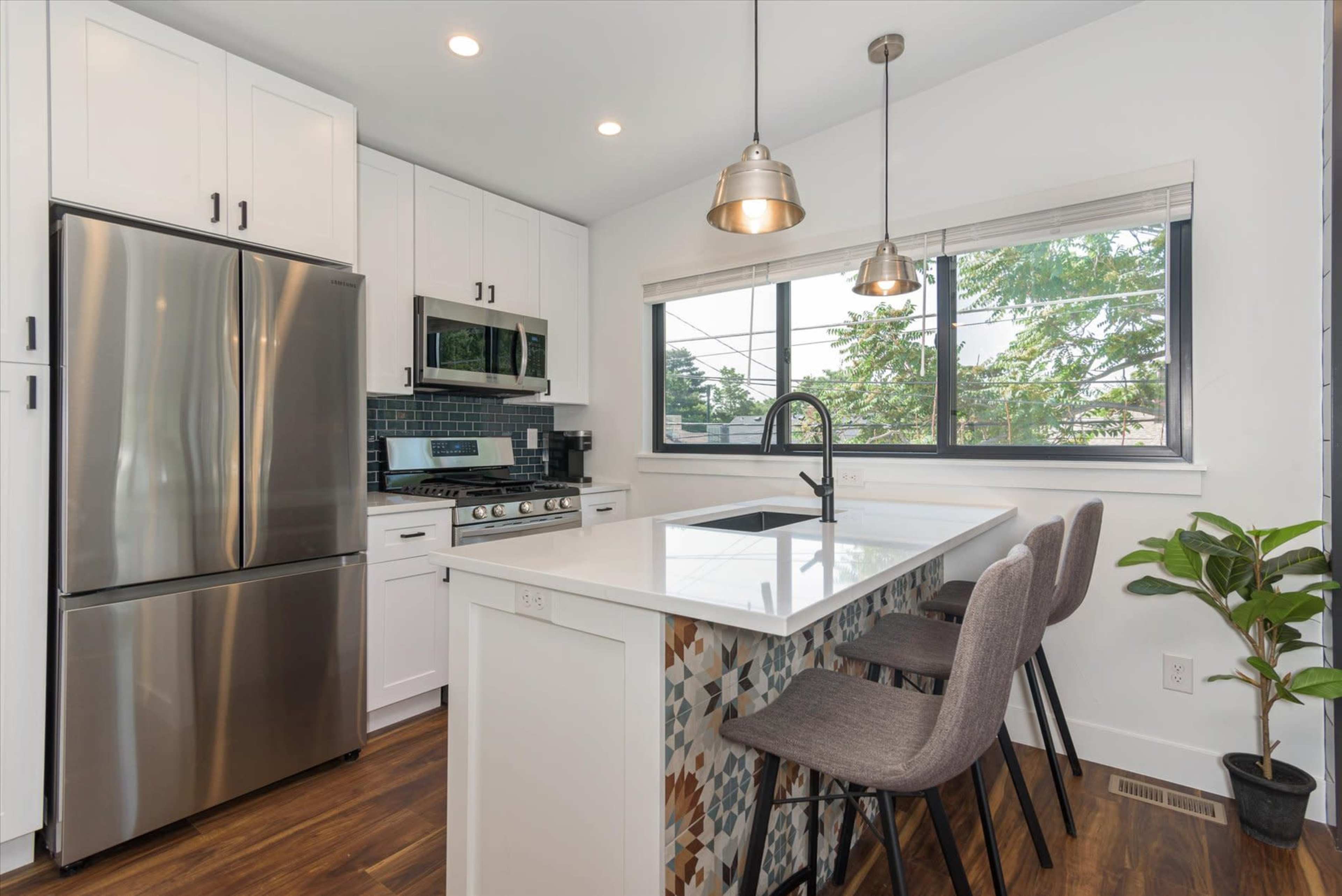 A modern kitchen features stainless steel appliances, white cabinetry, and a centered island with three bar stools.