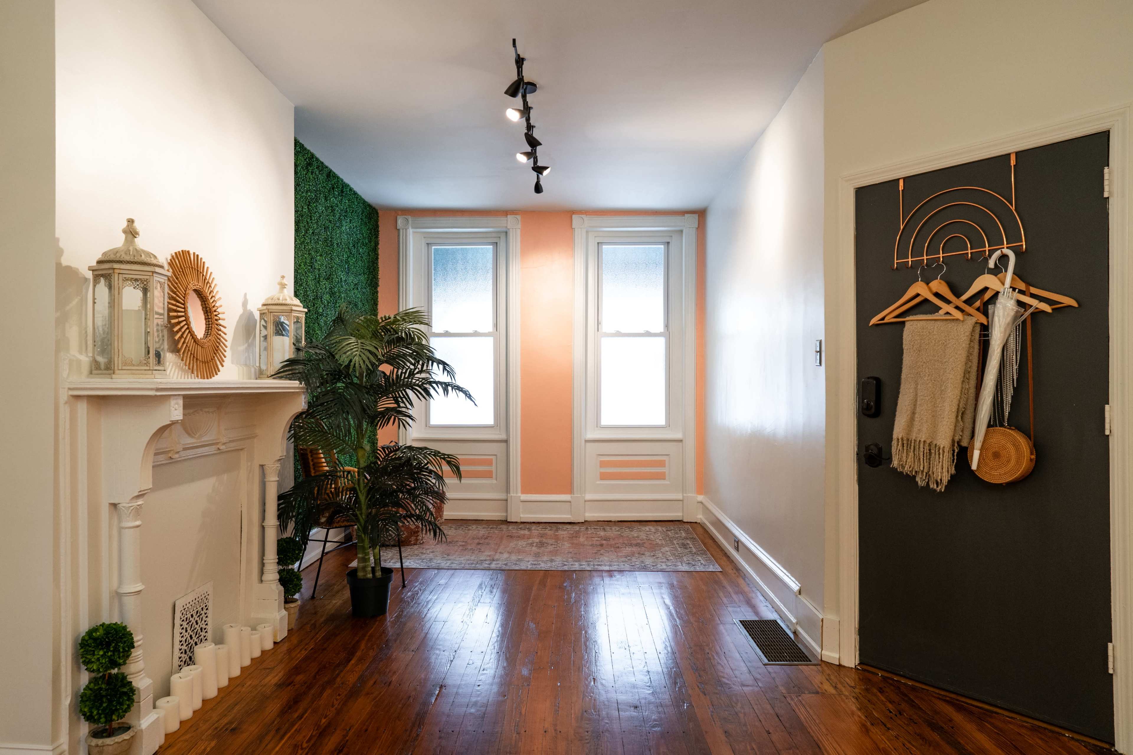 A bright hallway with a fireplace, two windows, a green accent wall, and a dark door adorned with decorative hooks.