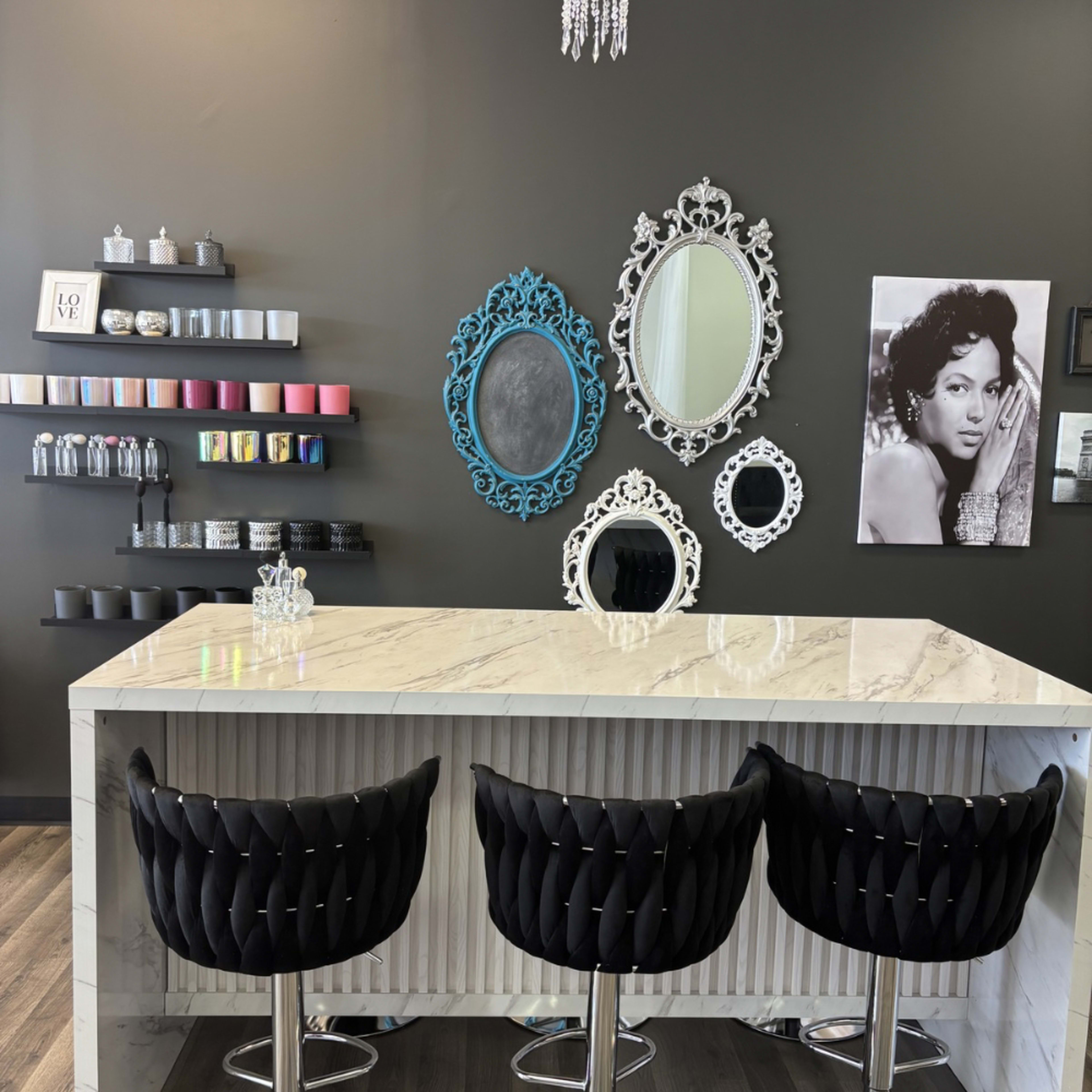 The image shows a modern interior featuring a marble-topped bar with three black upholstered stools, against a dark wall adorned with decorative mirrors and a framed black-and-white photo.