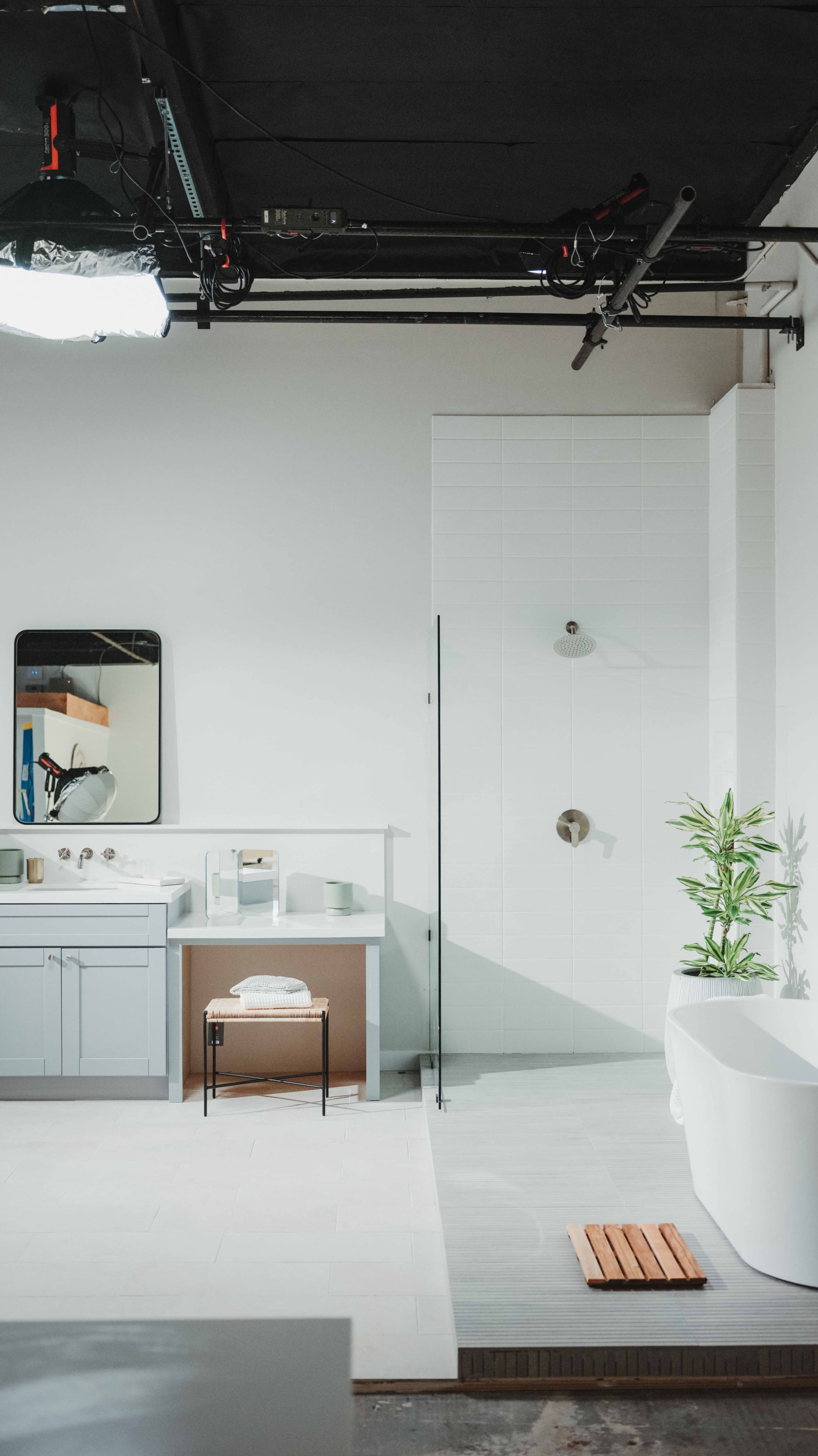 A modern bathroom featuring a shower, a freestanding tub, a sink with cabinetry, and a large mirror, all set against a minimalist backdrop.