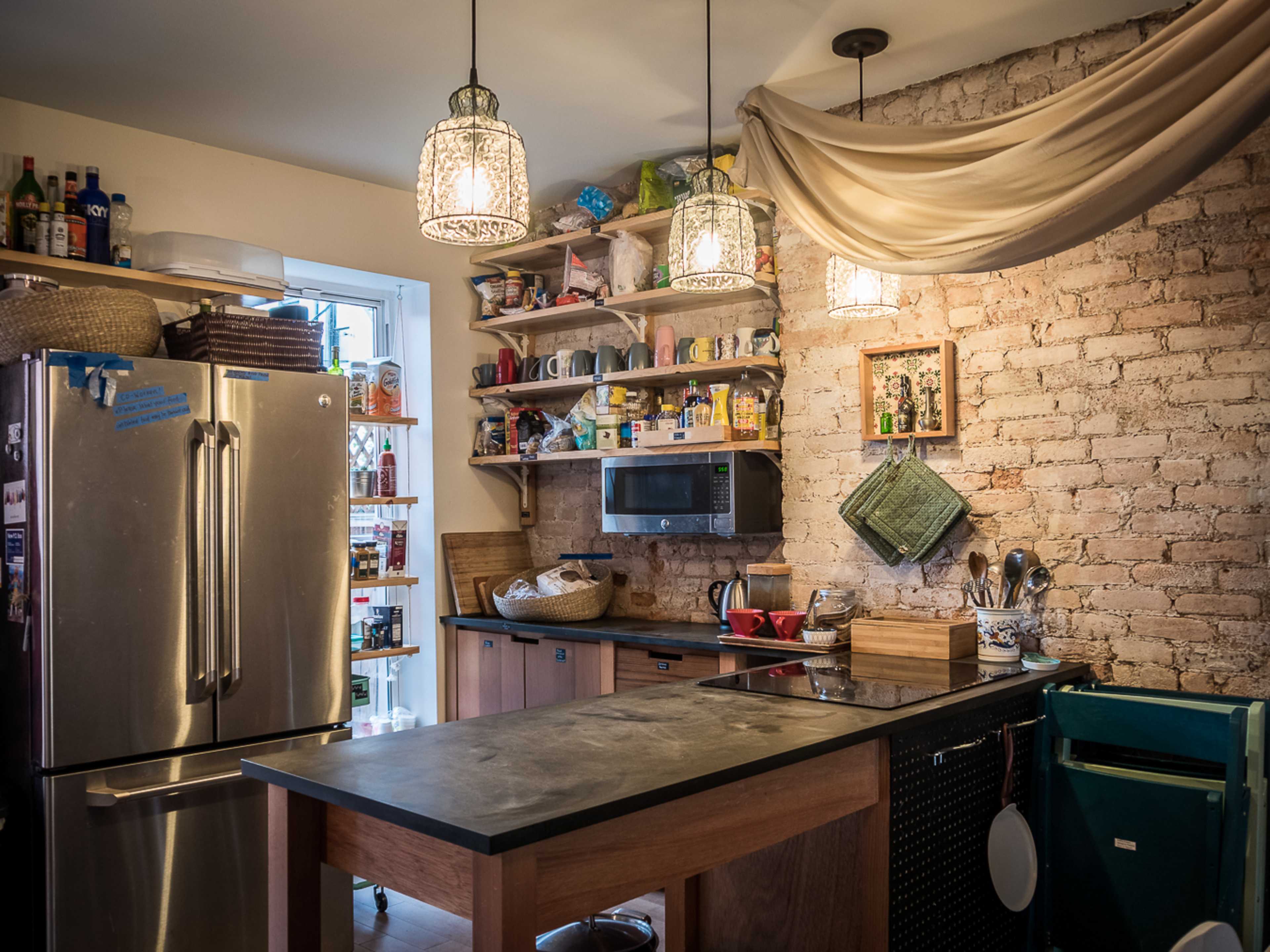A kitchen with a stainless steel refrigerator, wooden cabinets filled with colorful dishware, and three pendant lights hanging above a central island.