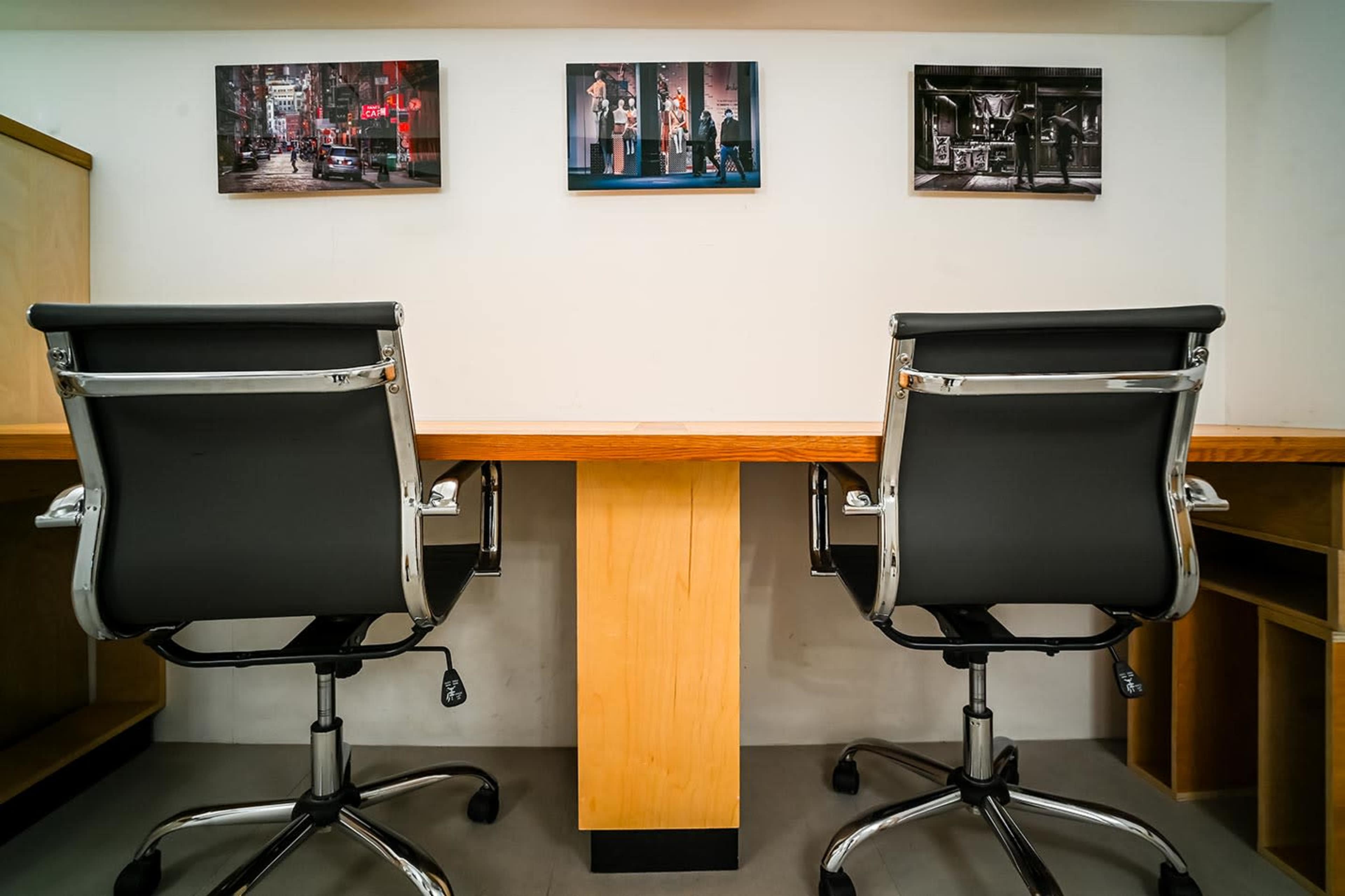 The image shows two modern office chairs positioned at a wooden desk with three framed photographs displayed on the wall above.