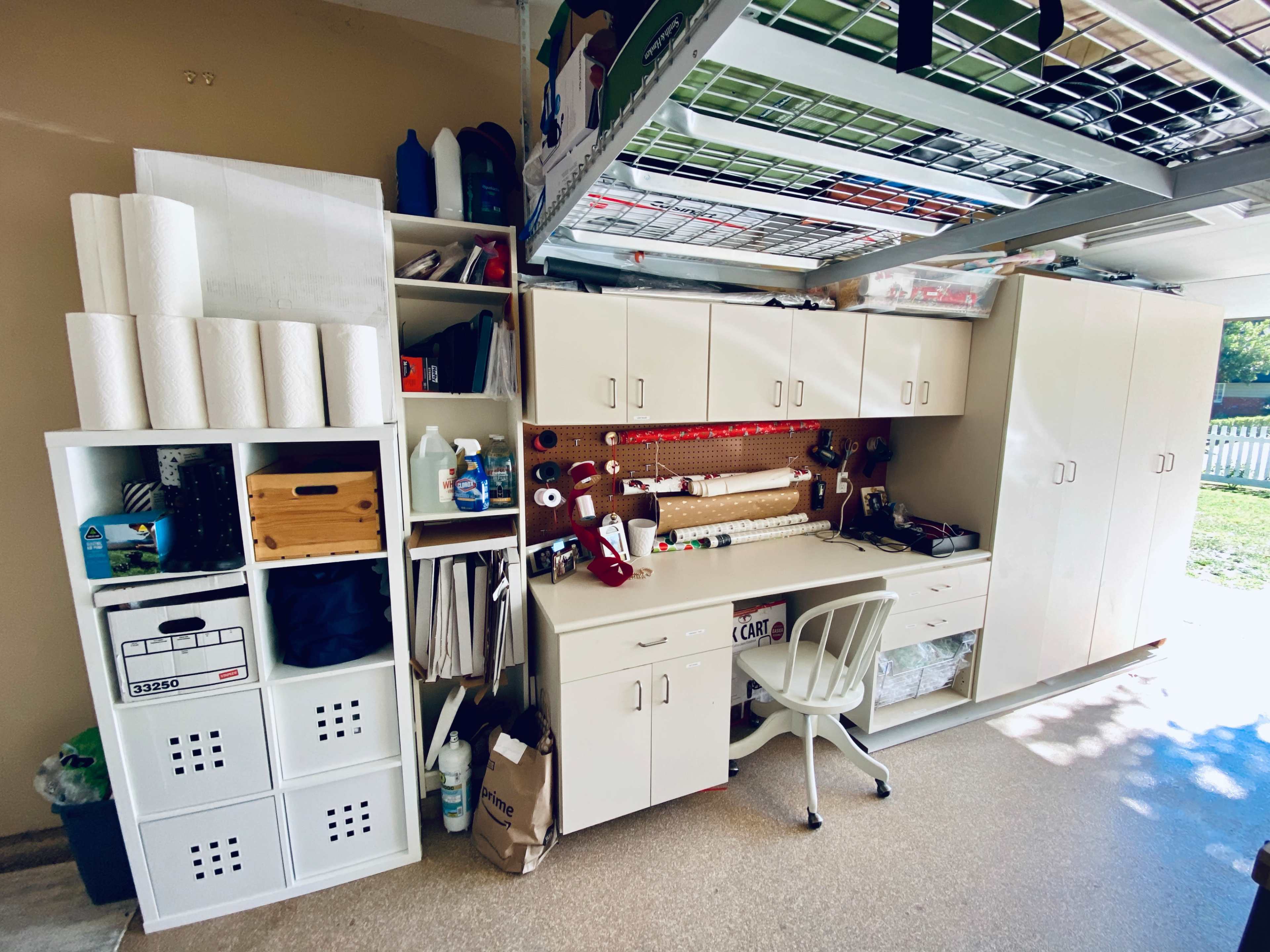 A neatly organized garage workspace with white cabinets, a desk, and storage units filled with supplies.
