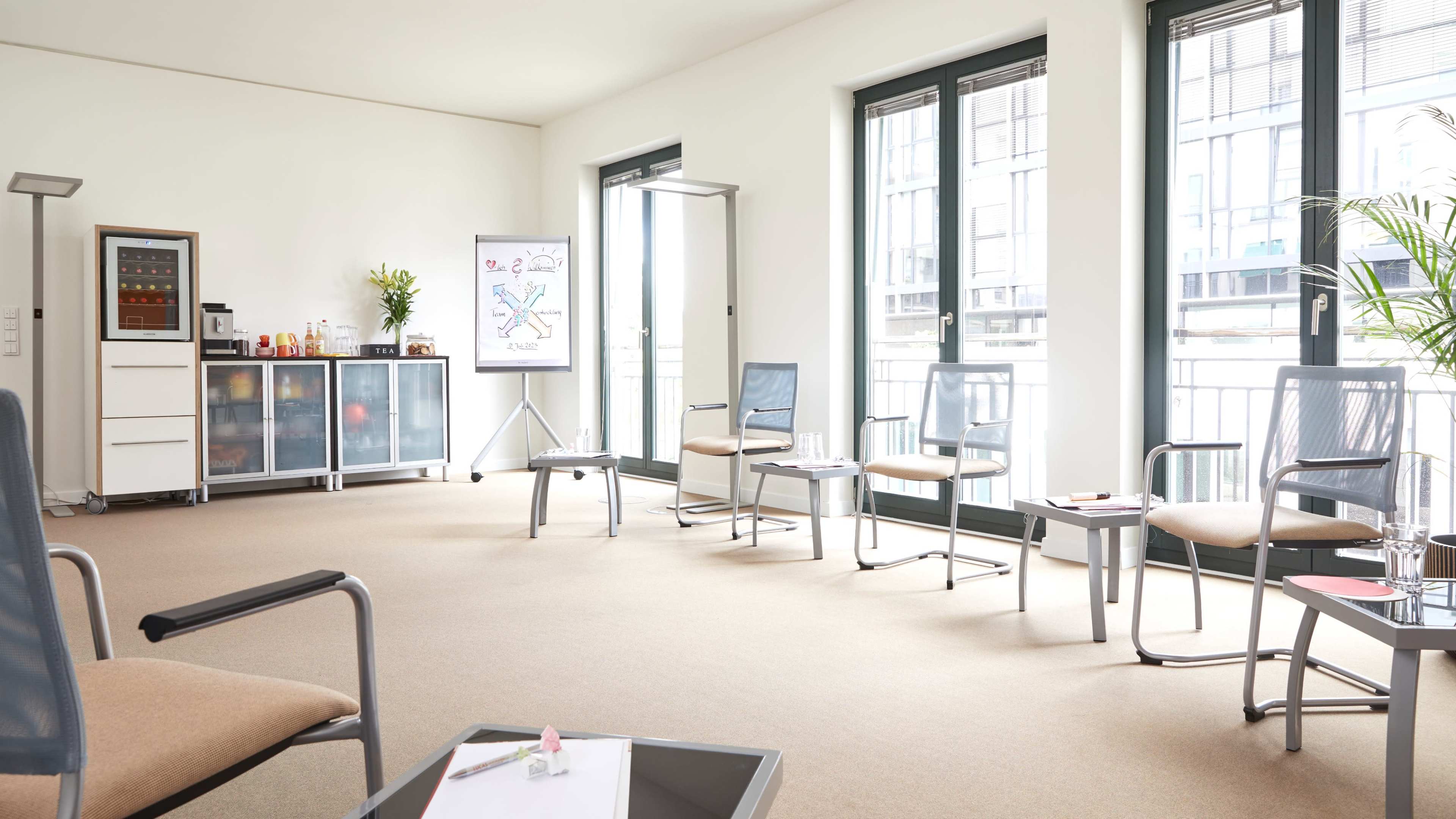 A bright, spacious waiting room with several chairs arranged around a coffee table, a presentation board, and storage cabinets.