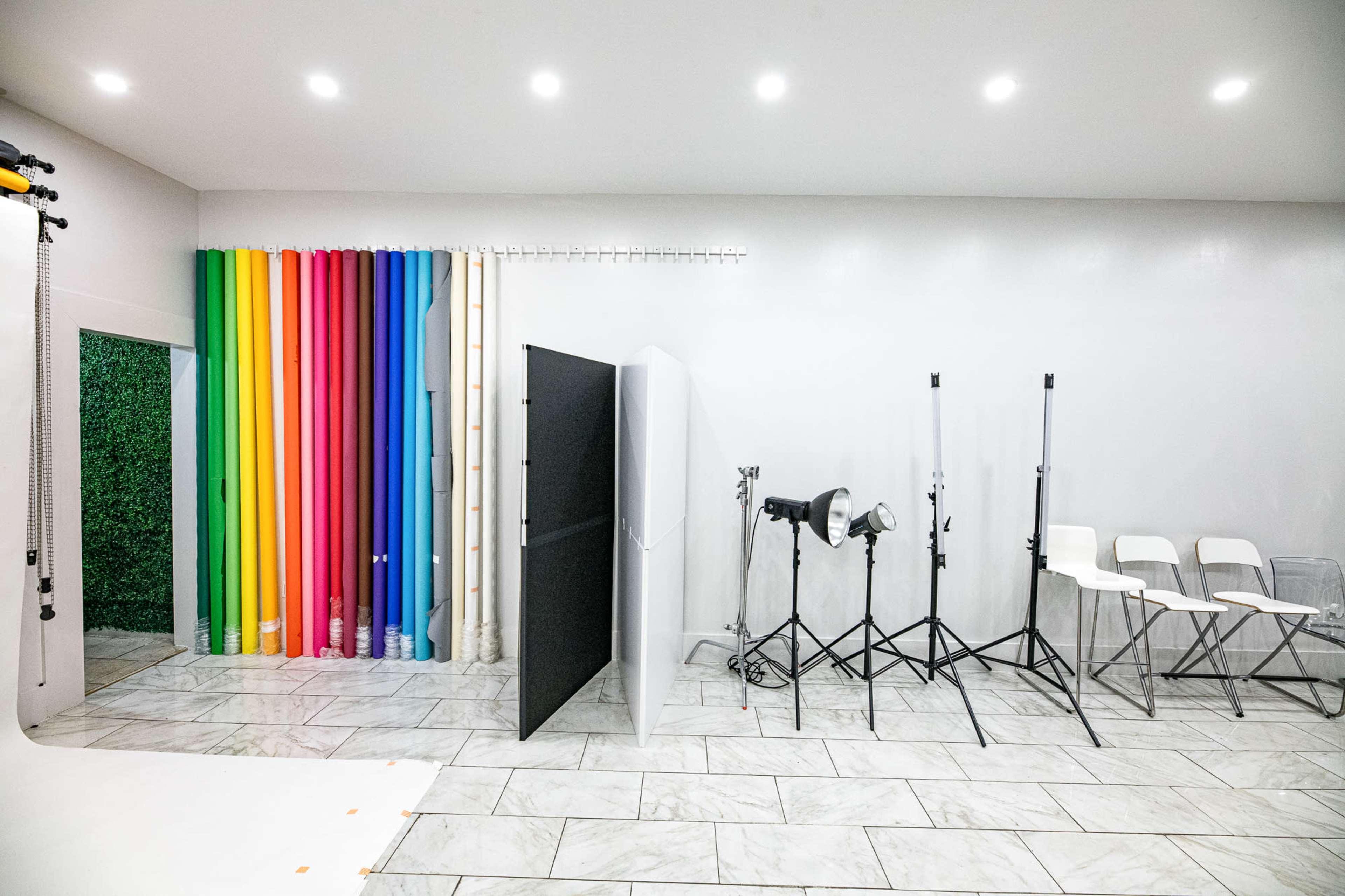 A photography studio featuring colorful backdrops, lighting equipment on stands, and a clean tiled floor.