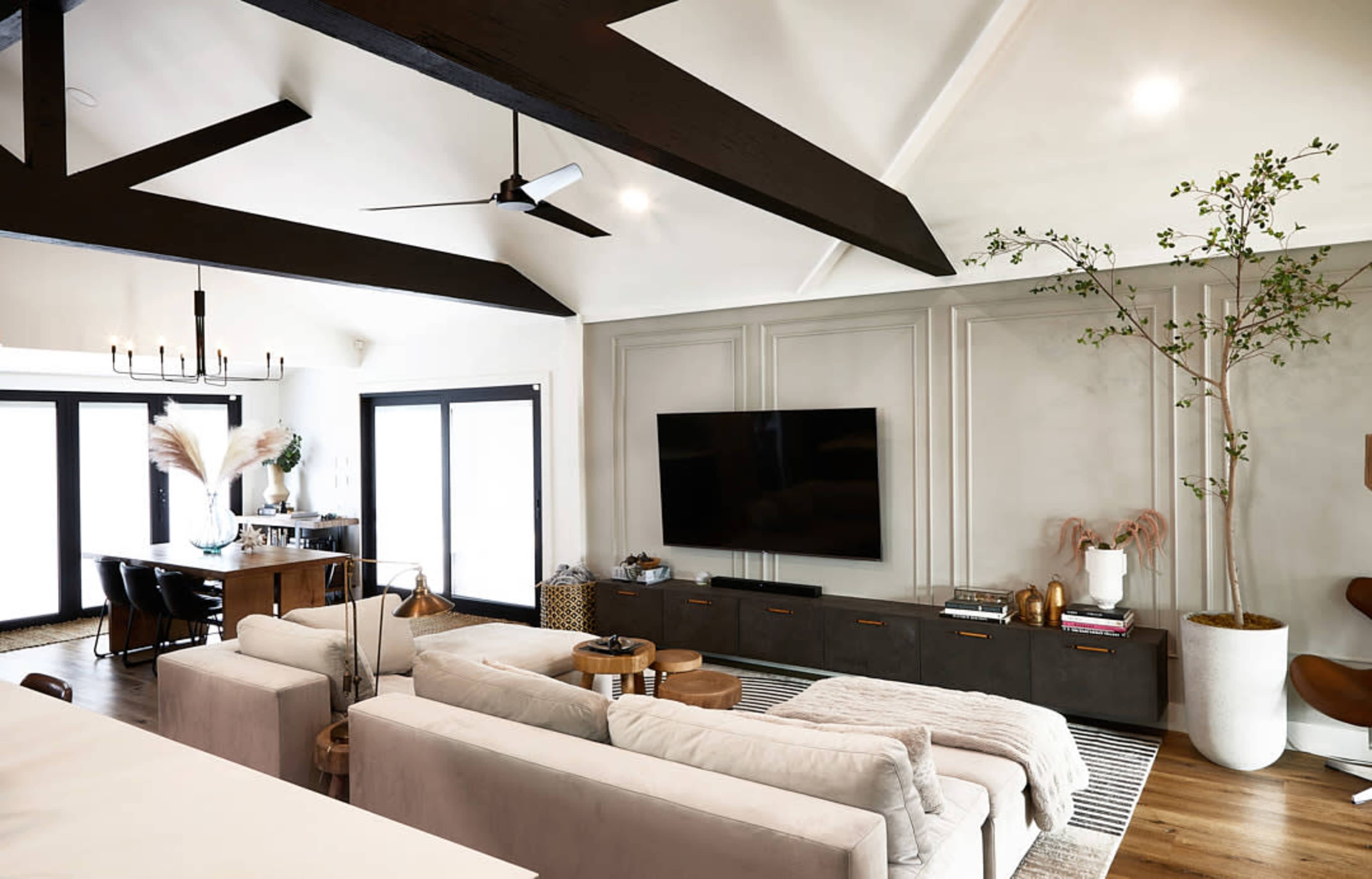 The living room features a spacious layout with a sectional sofa, a large television mounted on a feature wall, and a dining area with a table under a chandelier.