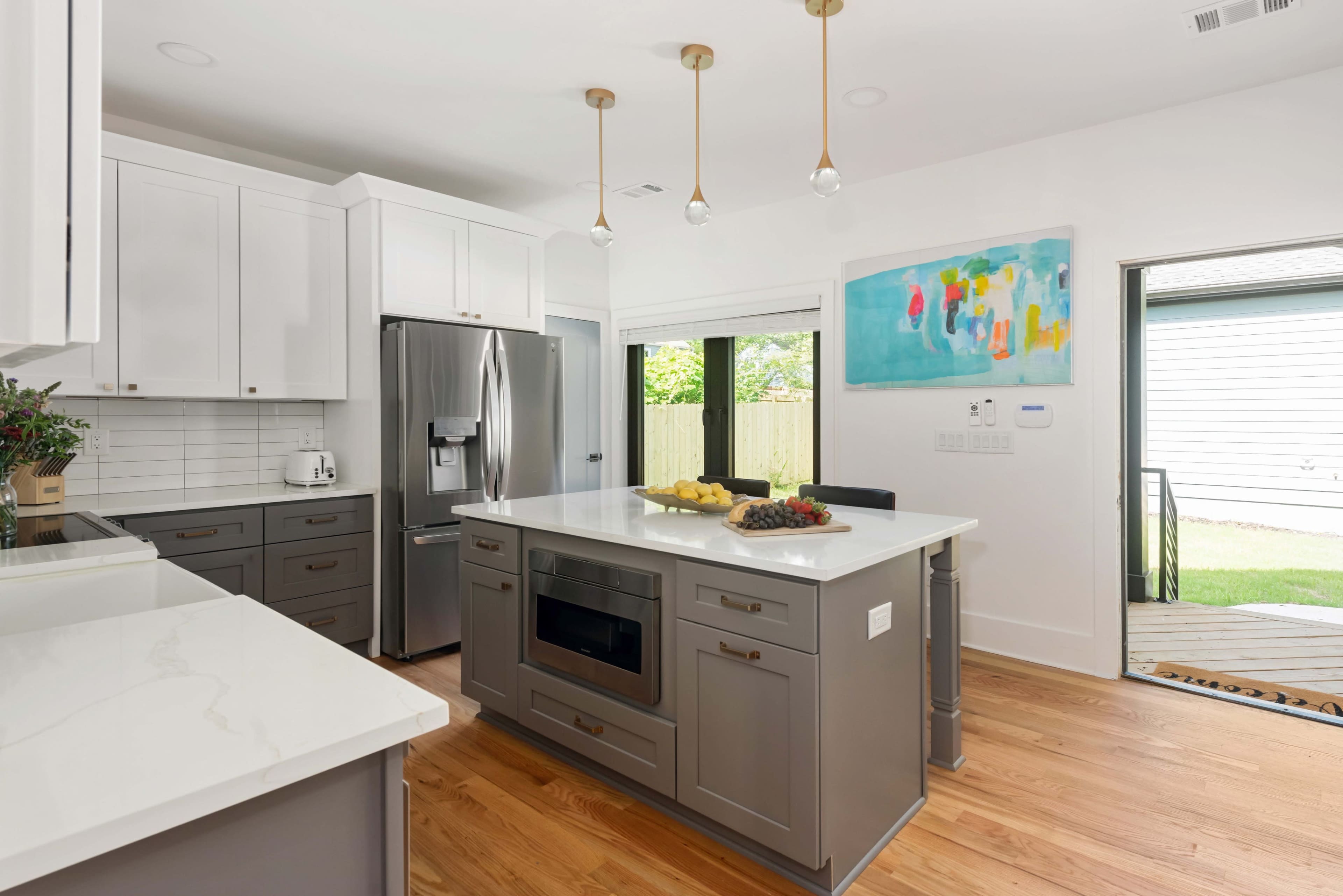A modern kitchen features white cabinetry, a gray island with a built-in microwave, and an open door leading to an outdoor area.