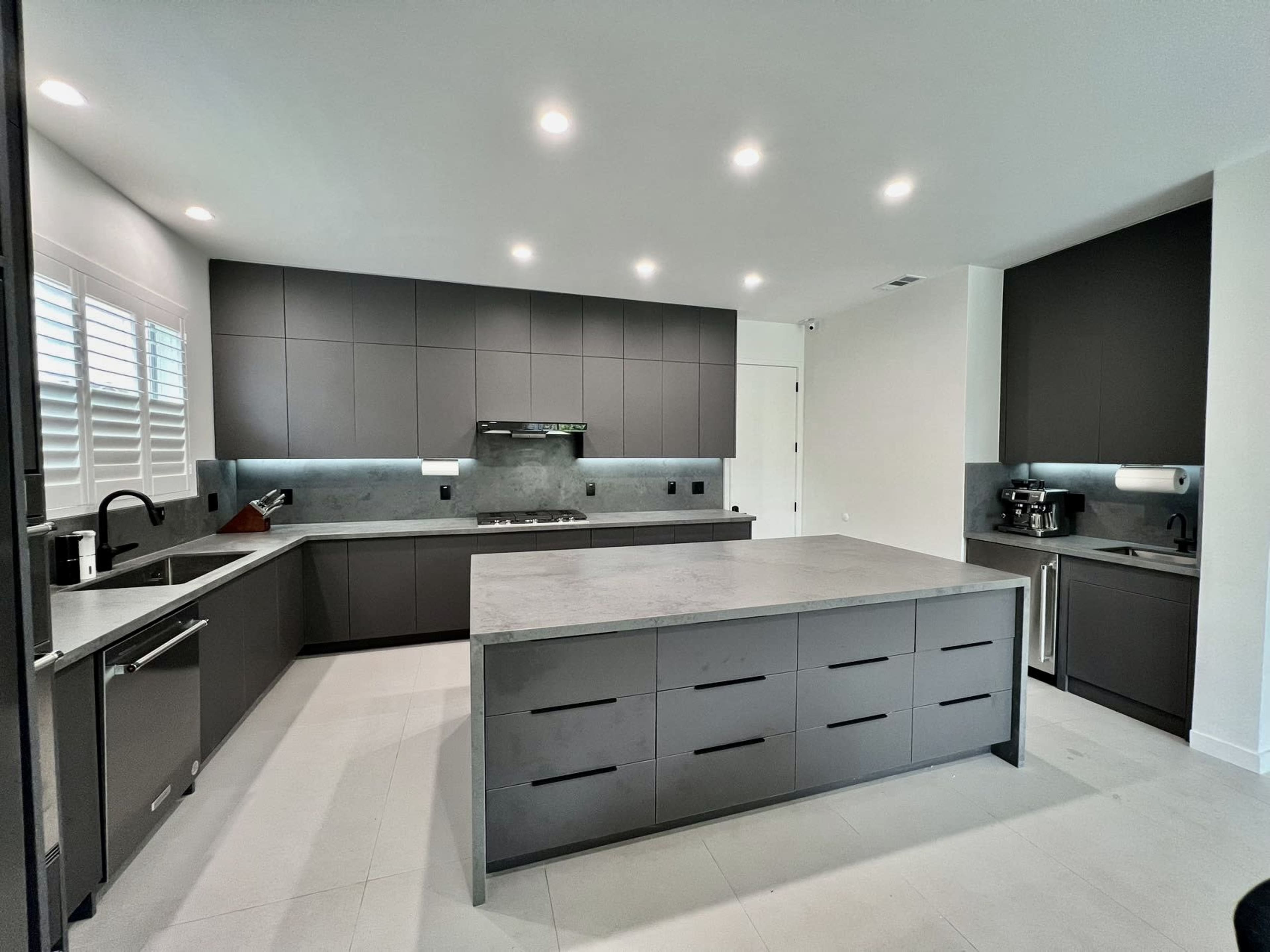 A modern kitchen featuring dark cabinets, a concrete island, and recessed lighting.