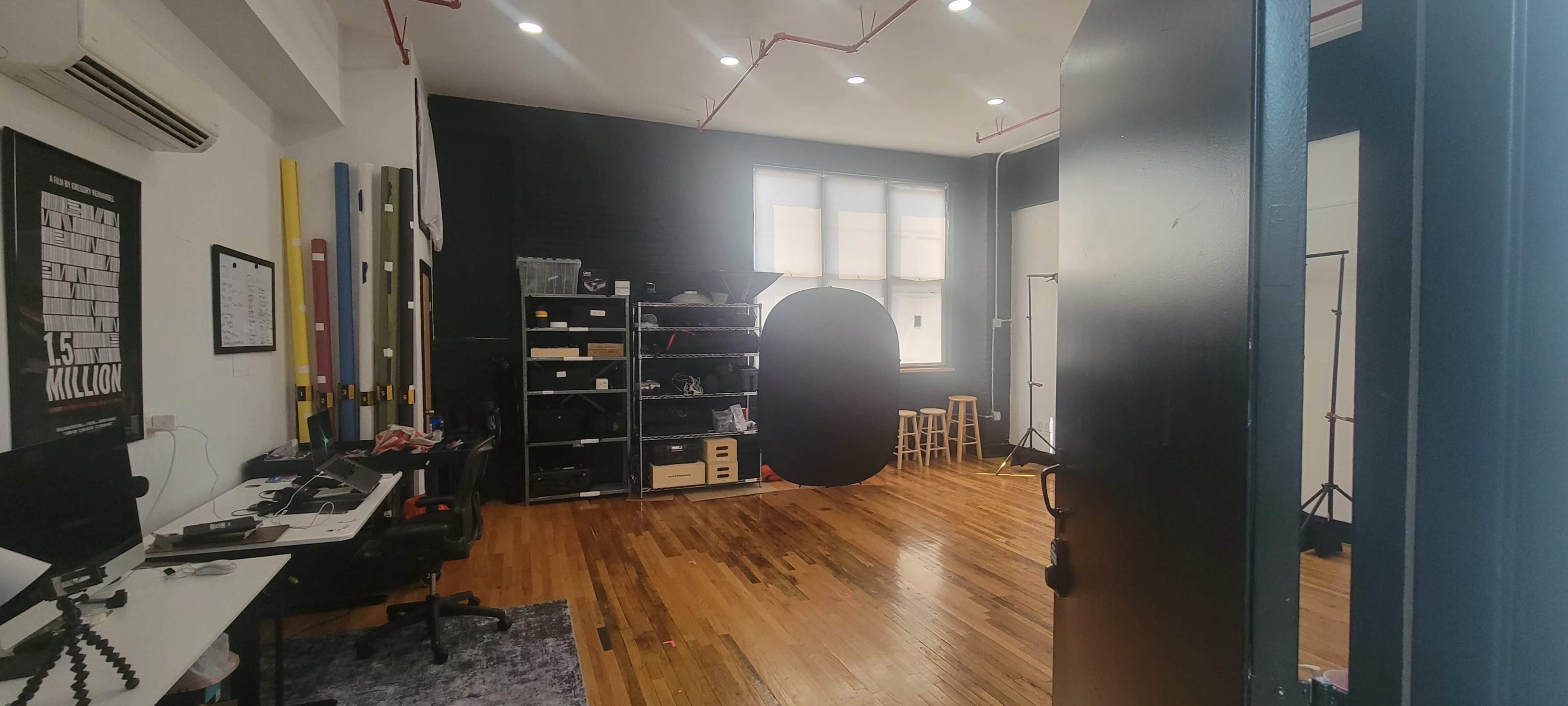 A studio space with wooden floors, a black wall featuring an oval backdrop, shelves for storage, and a small seating area with stools.