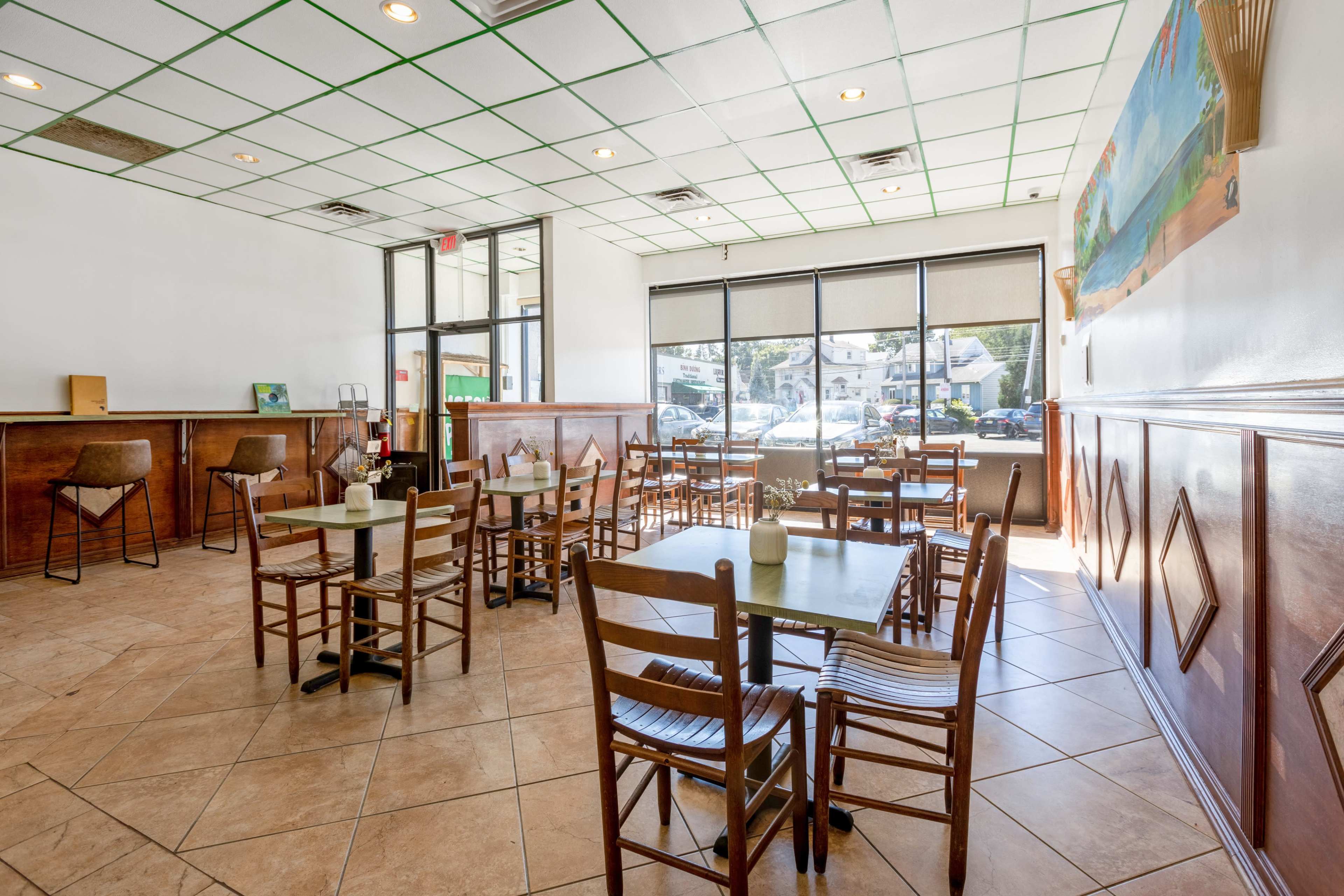 A bright, empty dining area of a restaurant with tables and chairs arranged neatly and large windows allowing natural light.