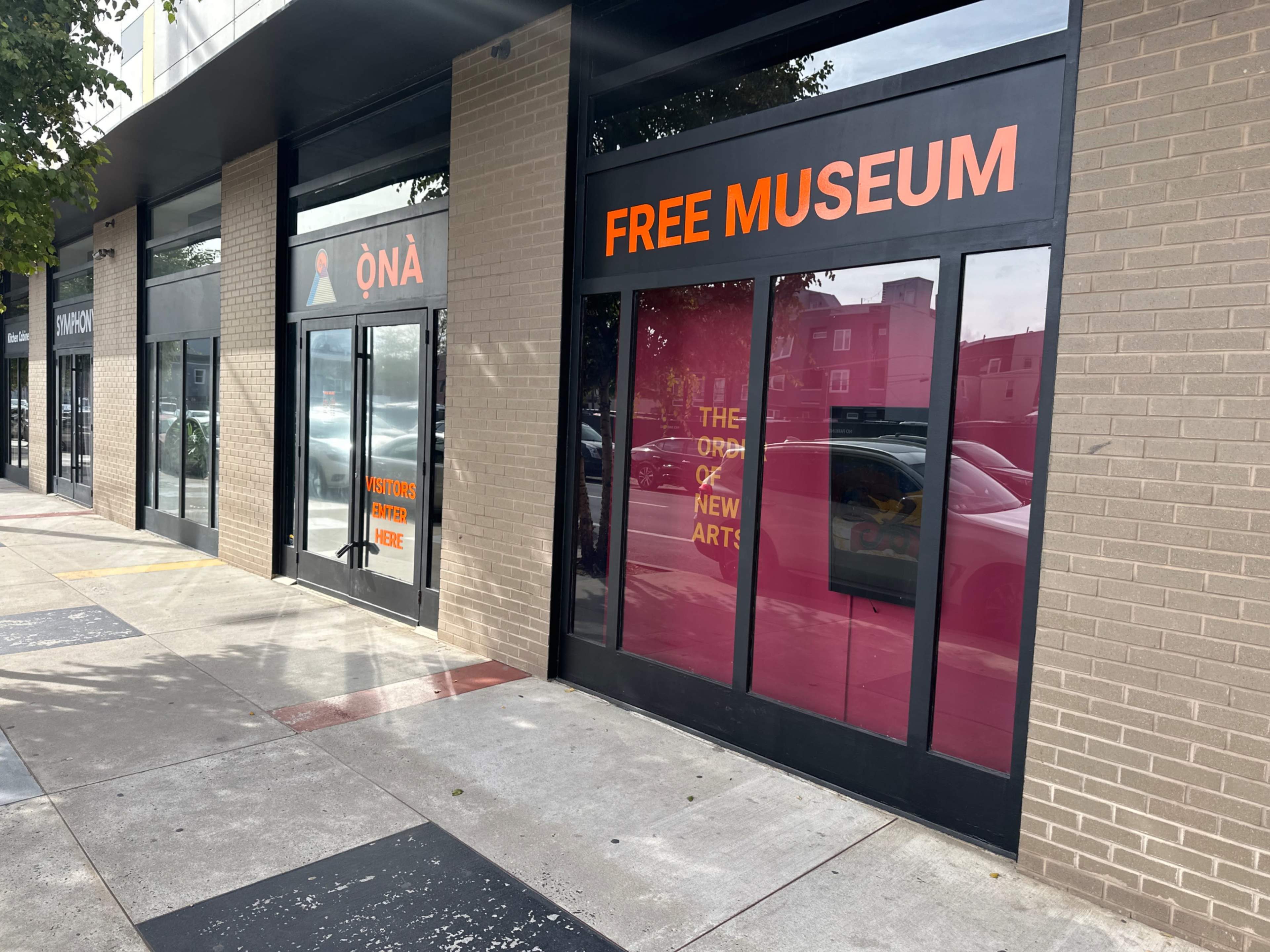 The image shows a row of storefronts, with one prominently displaying the text "FREE MUSEUM" in large orange letters on the glass door.