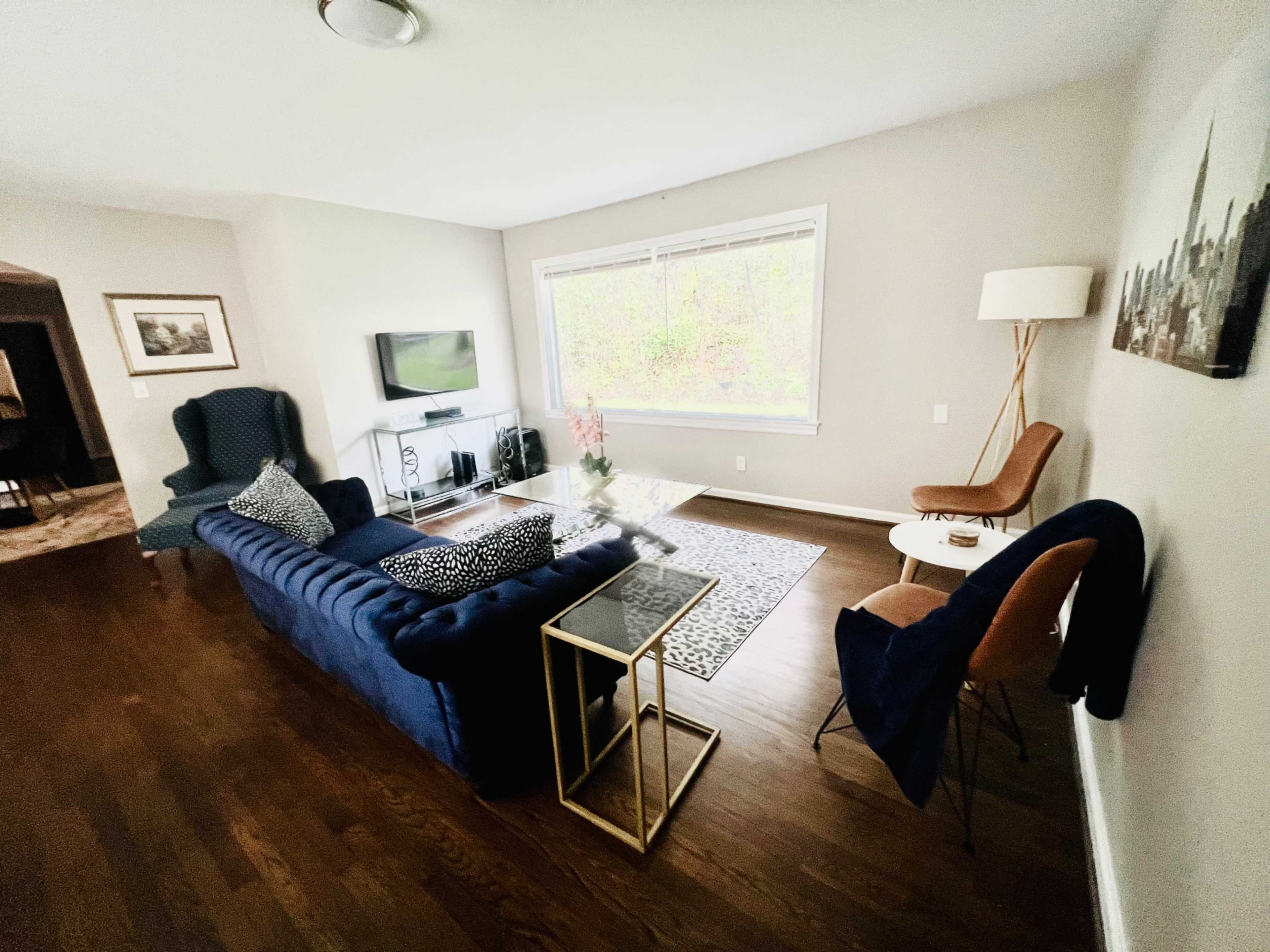 A modern living room features a blue sofa, wooden floor, television, and various furniture pieces arranged around a coffee table.
