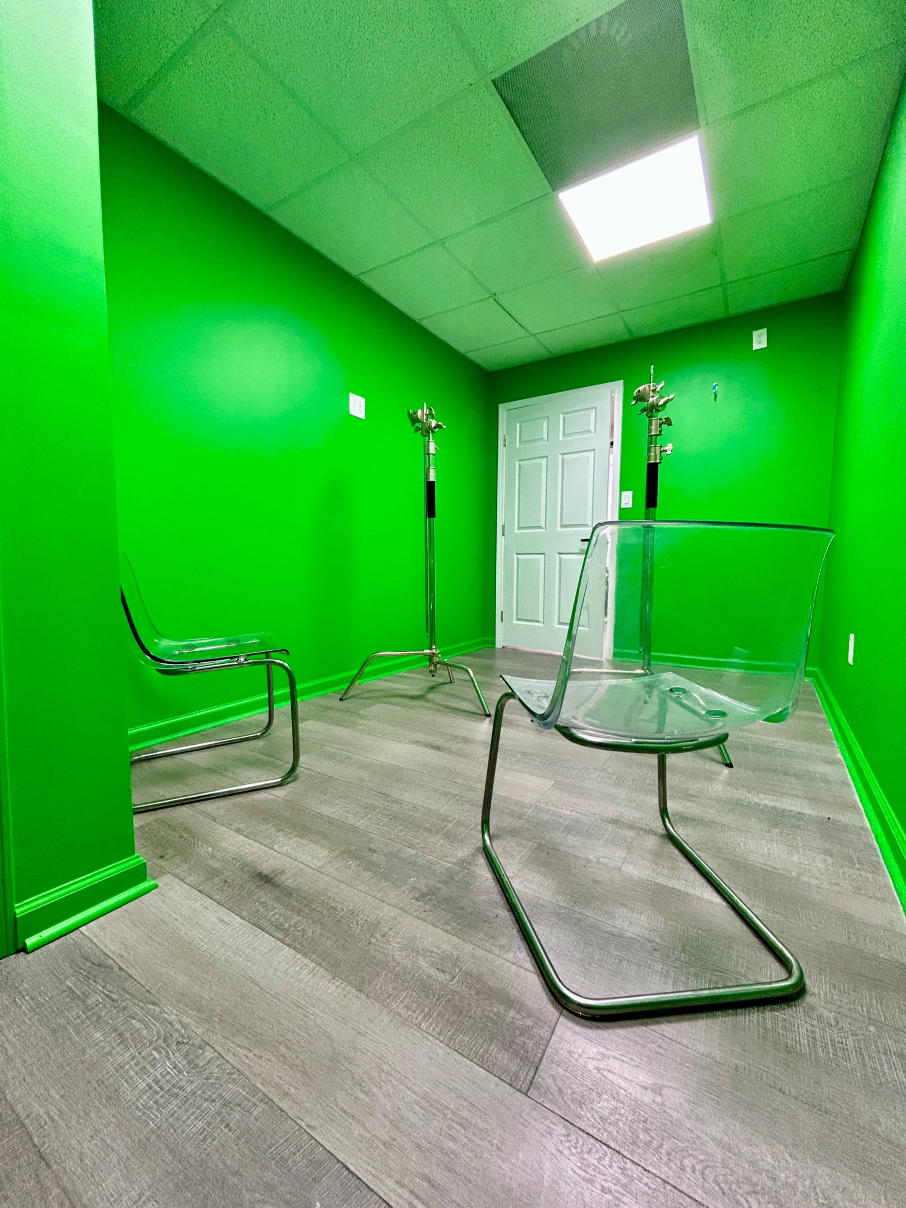 The image shows a small room with bright green walls, two clear acrylic chairs, and a door in the background.