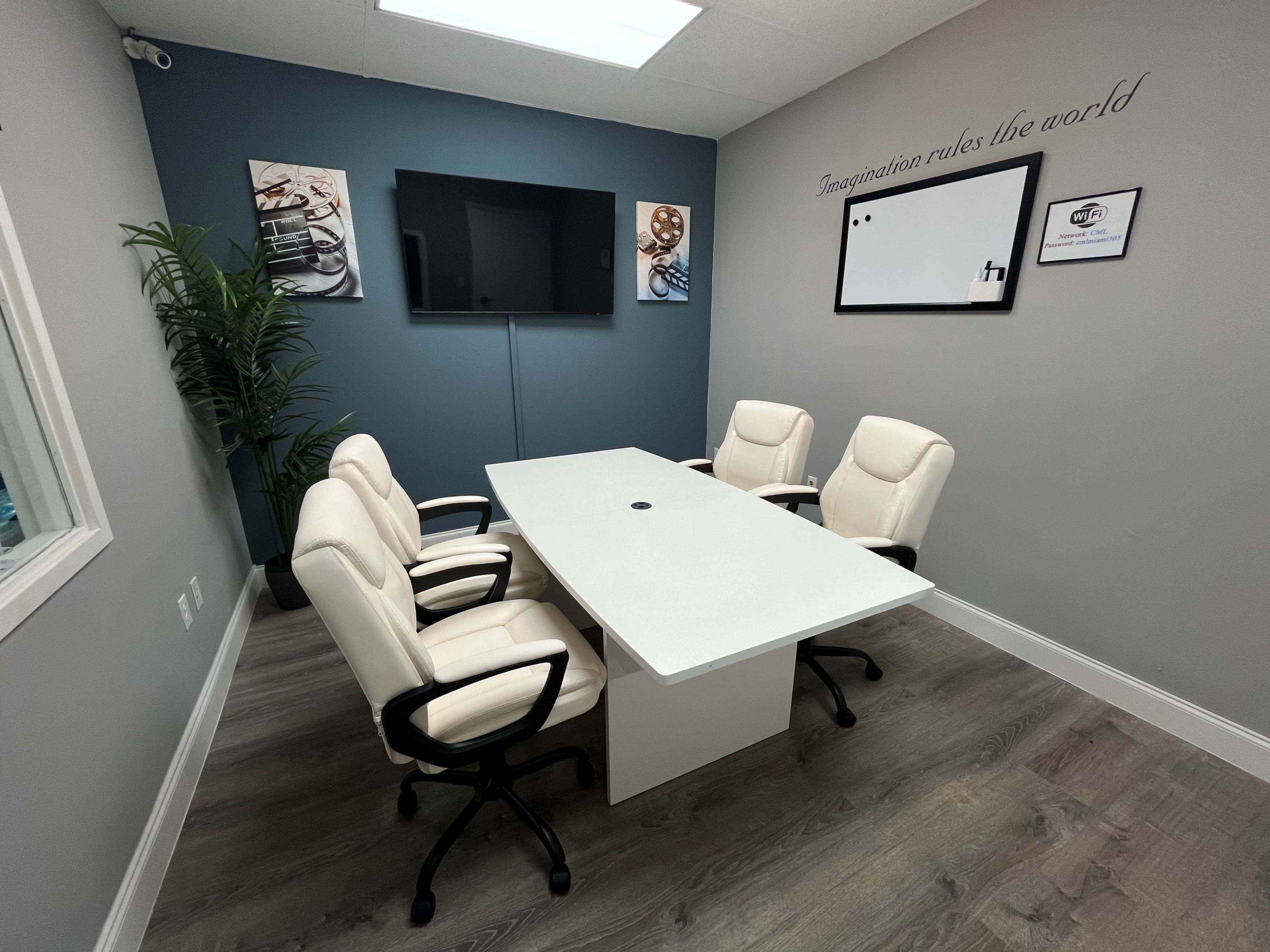 A modern conference room with a white oval table, four white office chairs, a television on the wall, and a decorative wall featuring a quote and artwork.