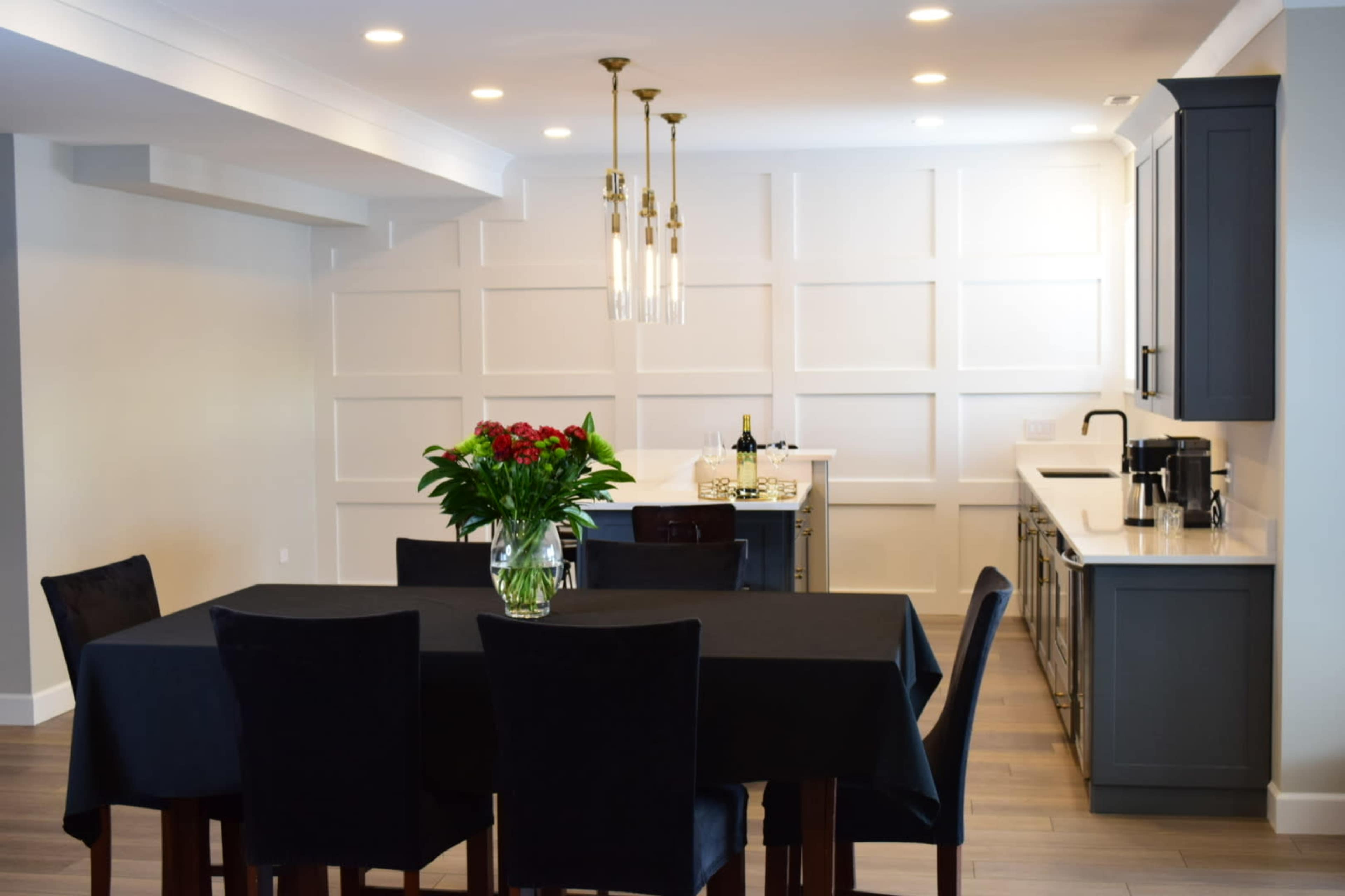 A modern dining area features a black table set with chairs, a vase of flowers, and a sleek kitchen in the background.