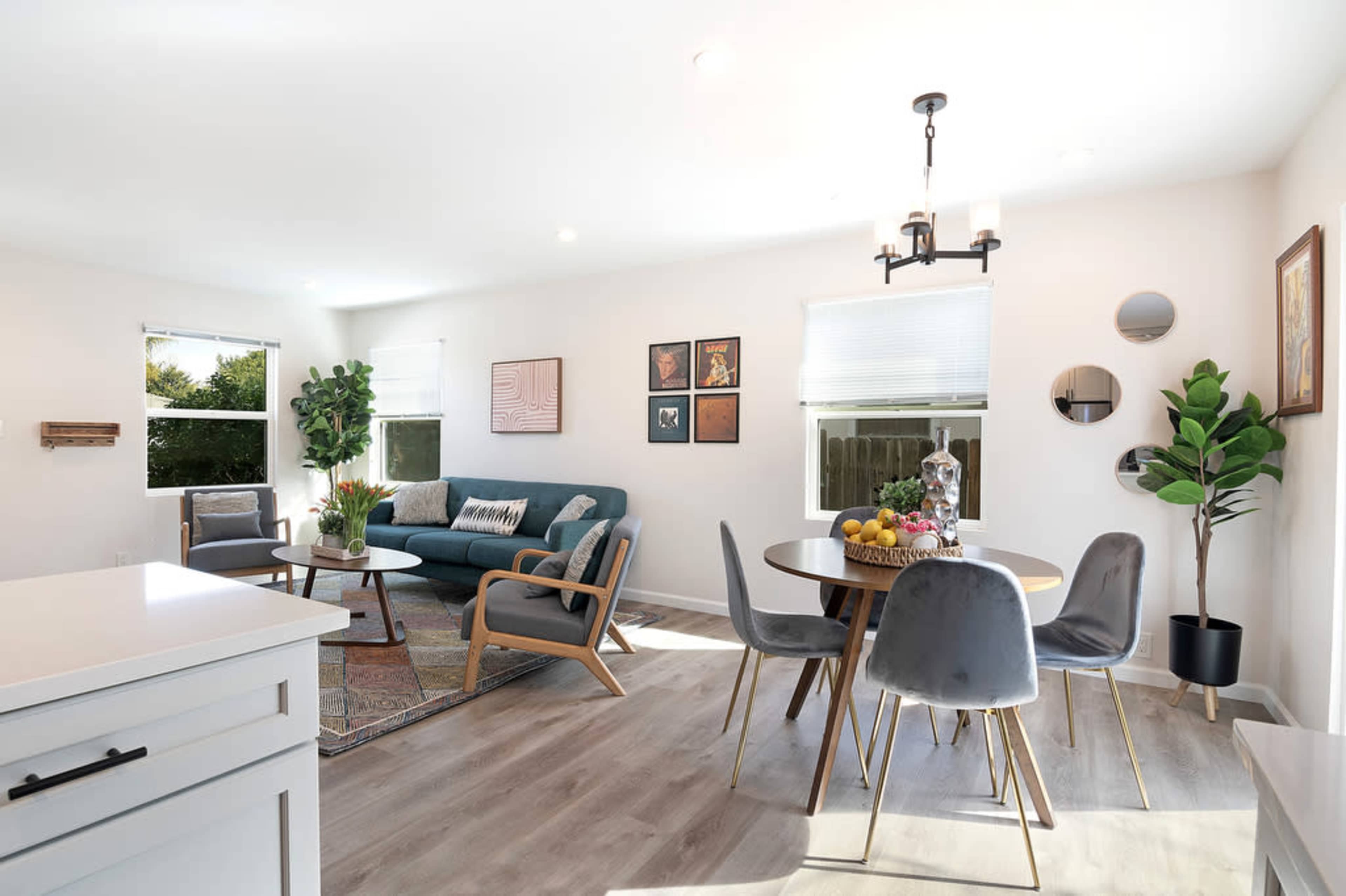 A bright, modern living space featuring a seating area with a green sofa, a round dining table, and decorative art on the walls.