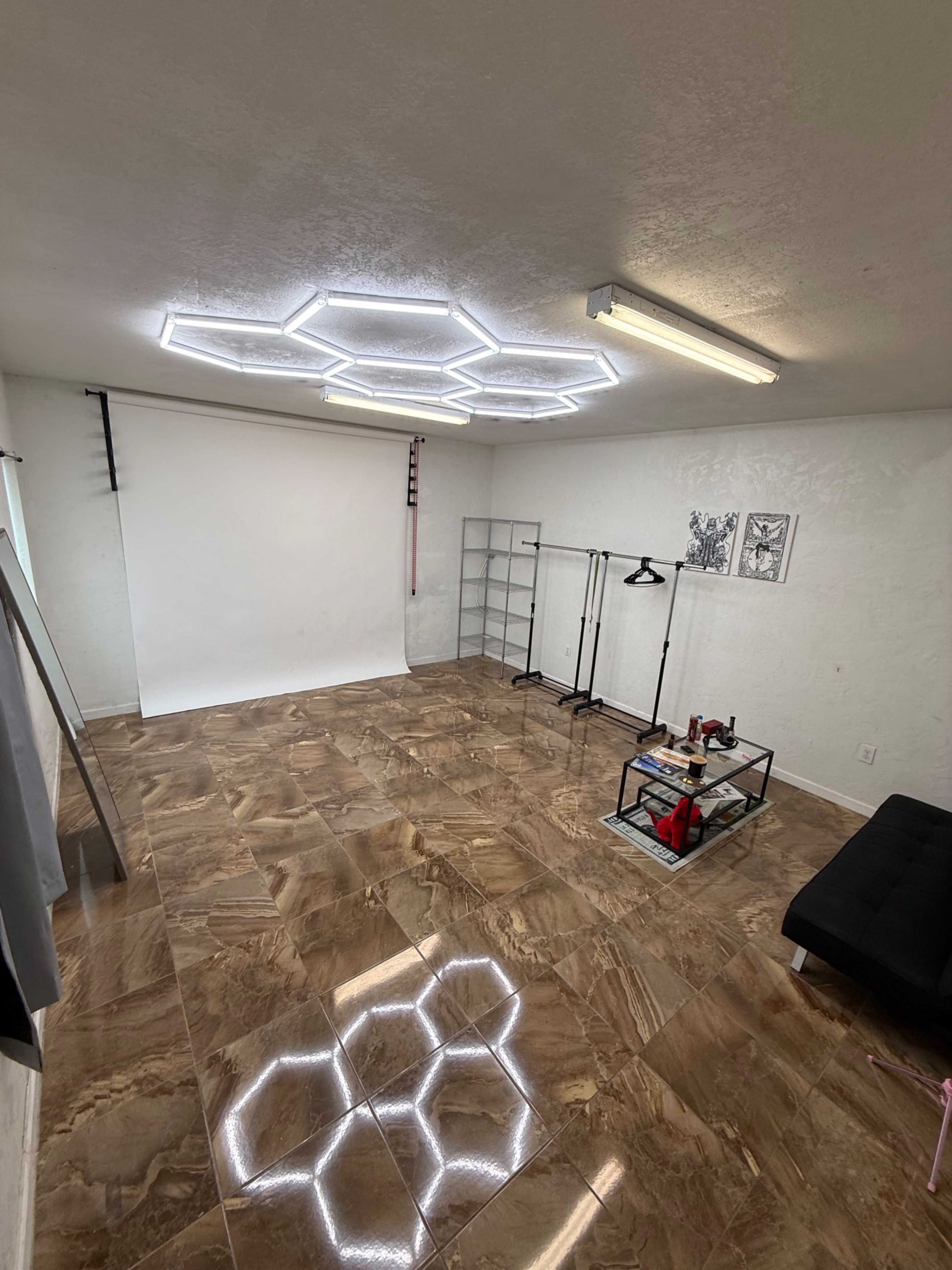 The image shows an empty photo studio with a tiled floor, a white backdrop, and modern lighting fixtures shaped like hexagons.