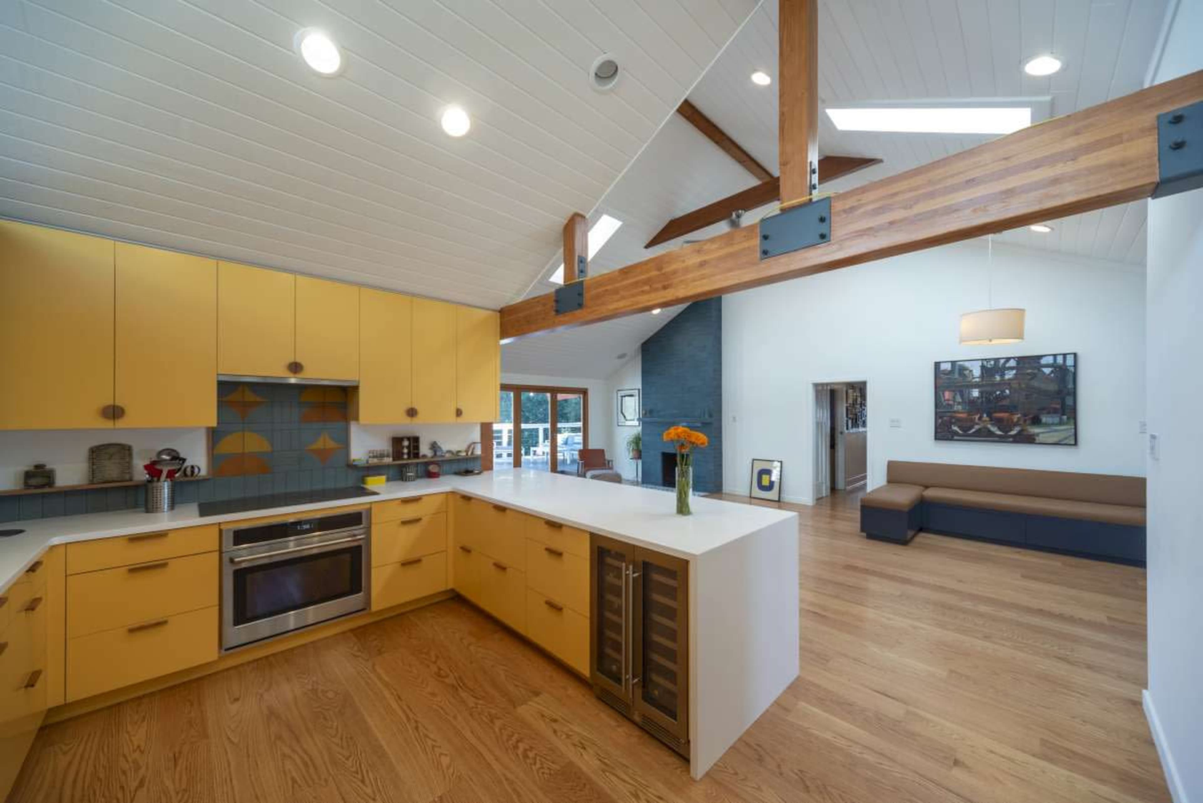 The image shows a modern kitchen with yellow cabinetry and a white countertop, connected to a living area featuring a sofa and blue accent walls.