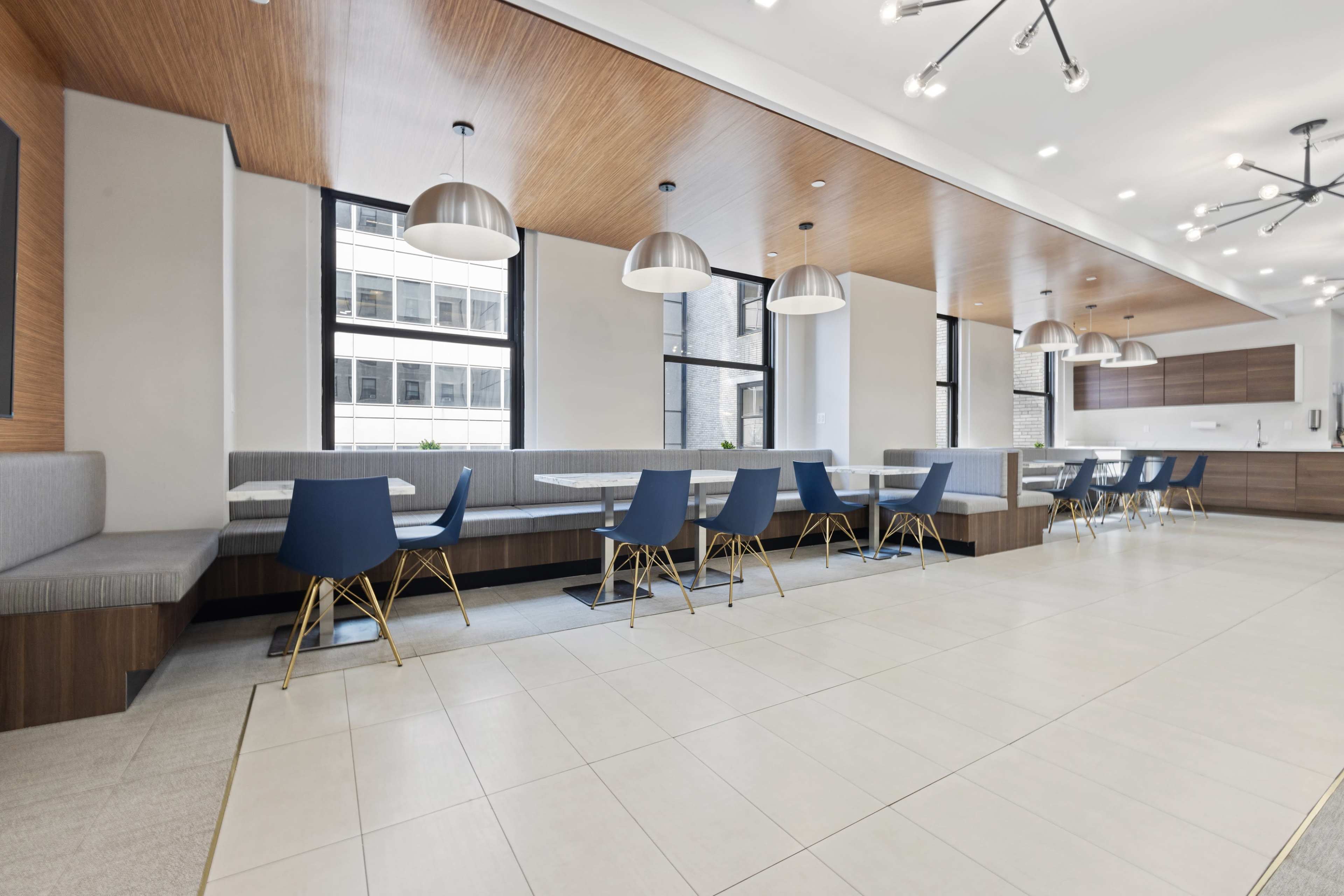 A modern dining area featuring multiple tables with blue chairs and pendant lighting, situated under a wooden ceiling.