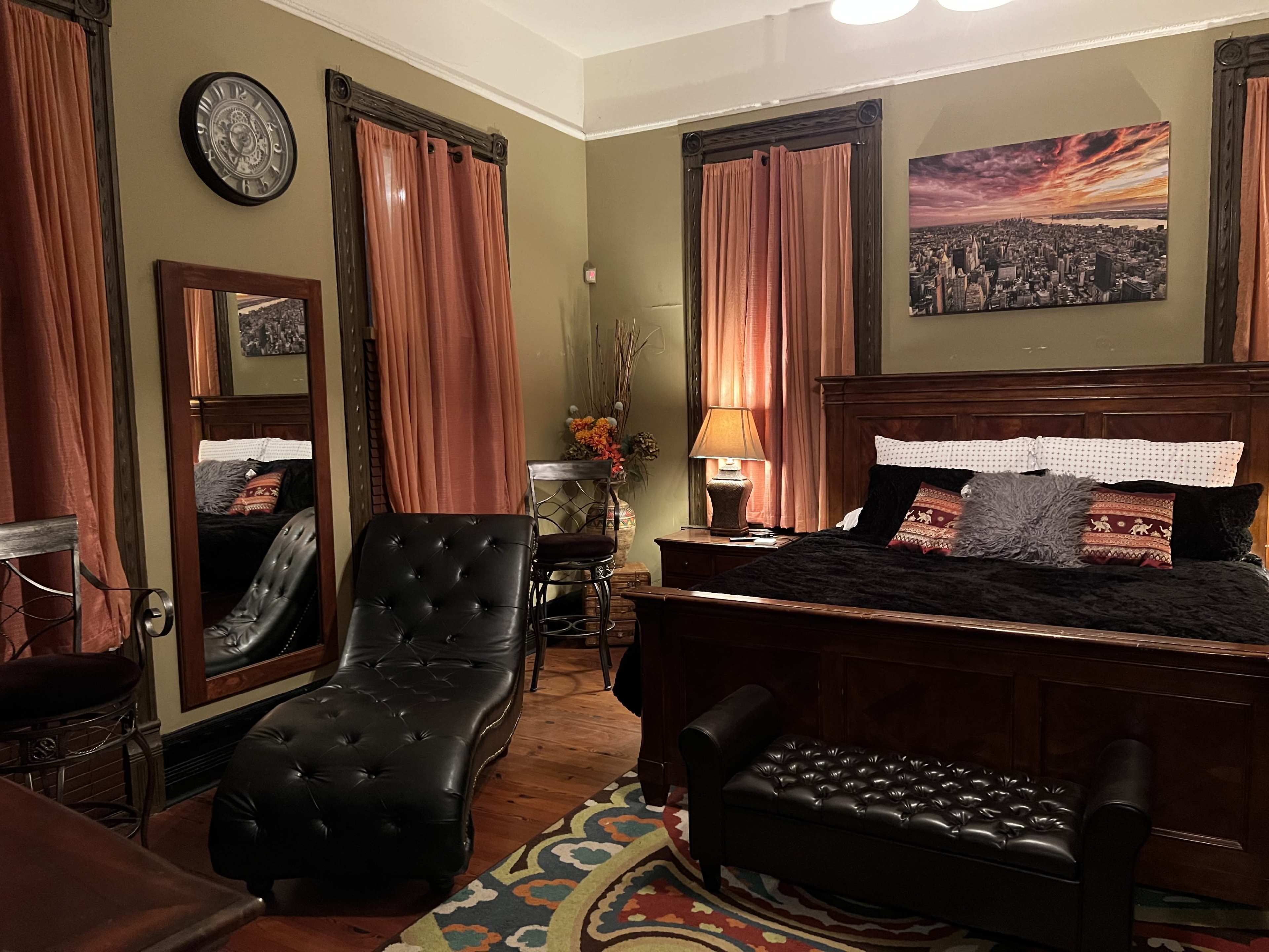 A cozy bedroom featuring a dark wooden bed, a mirrored dresser, a chaise lounge, and decorative curtains.
