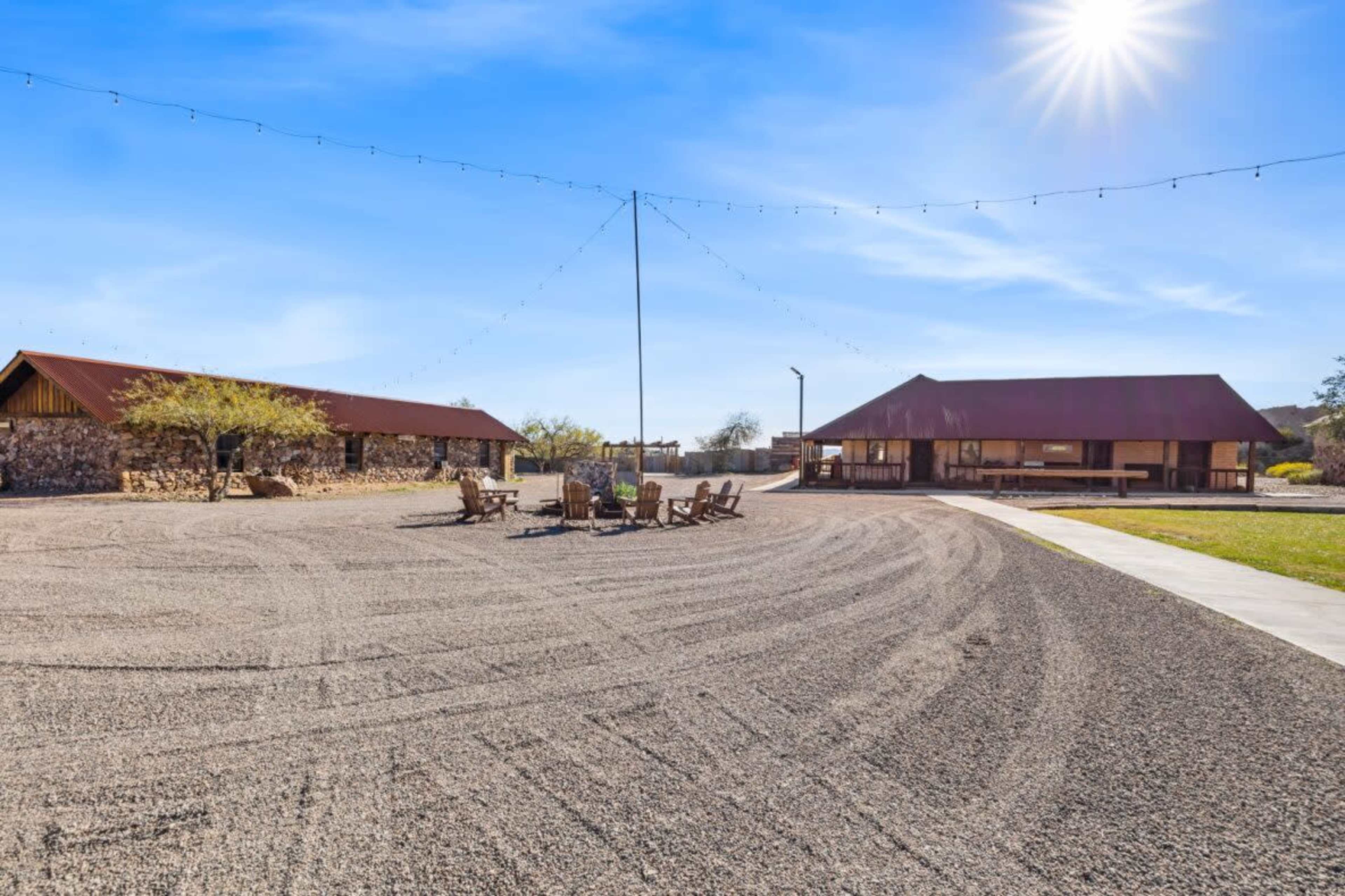 A spacious outdoor area features two structures with metal roofs, surrounded by a gravel surface and chairs arranged around a central point.