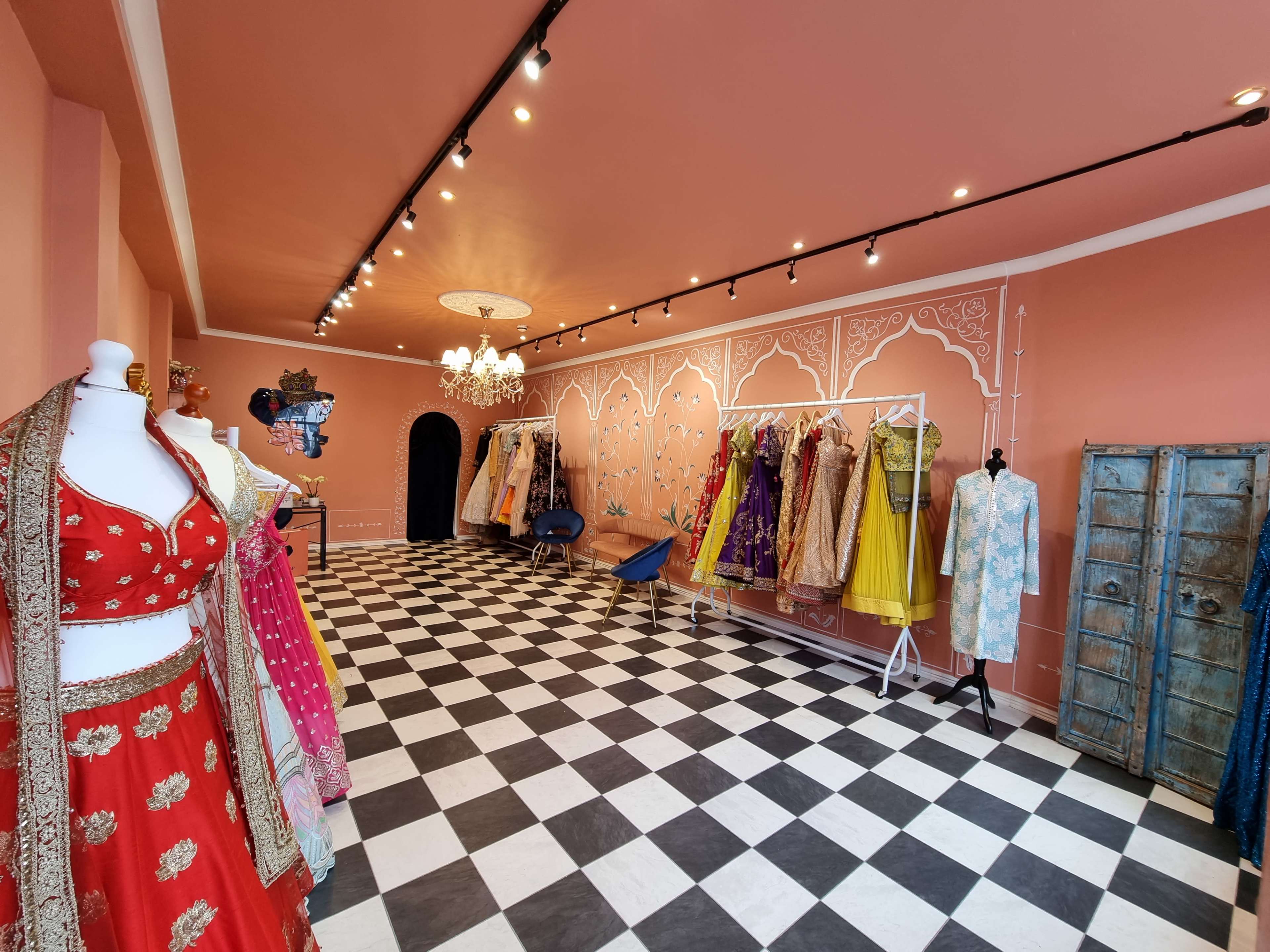 A boutique setting with a checkerboard floor, featuring colorful traditional garments displayed on racks and mannequins against a peach-colored wall.