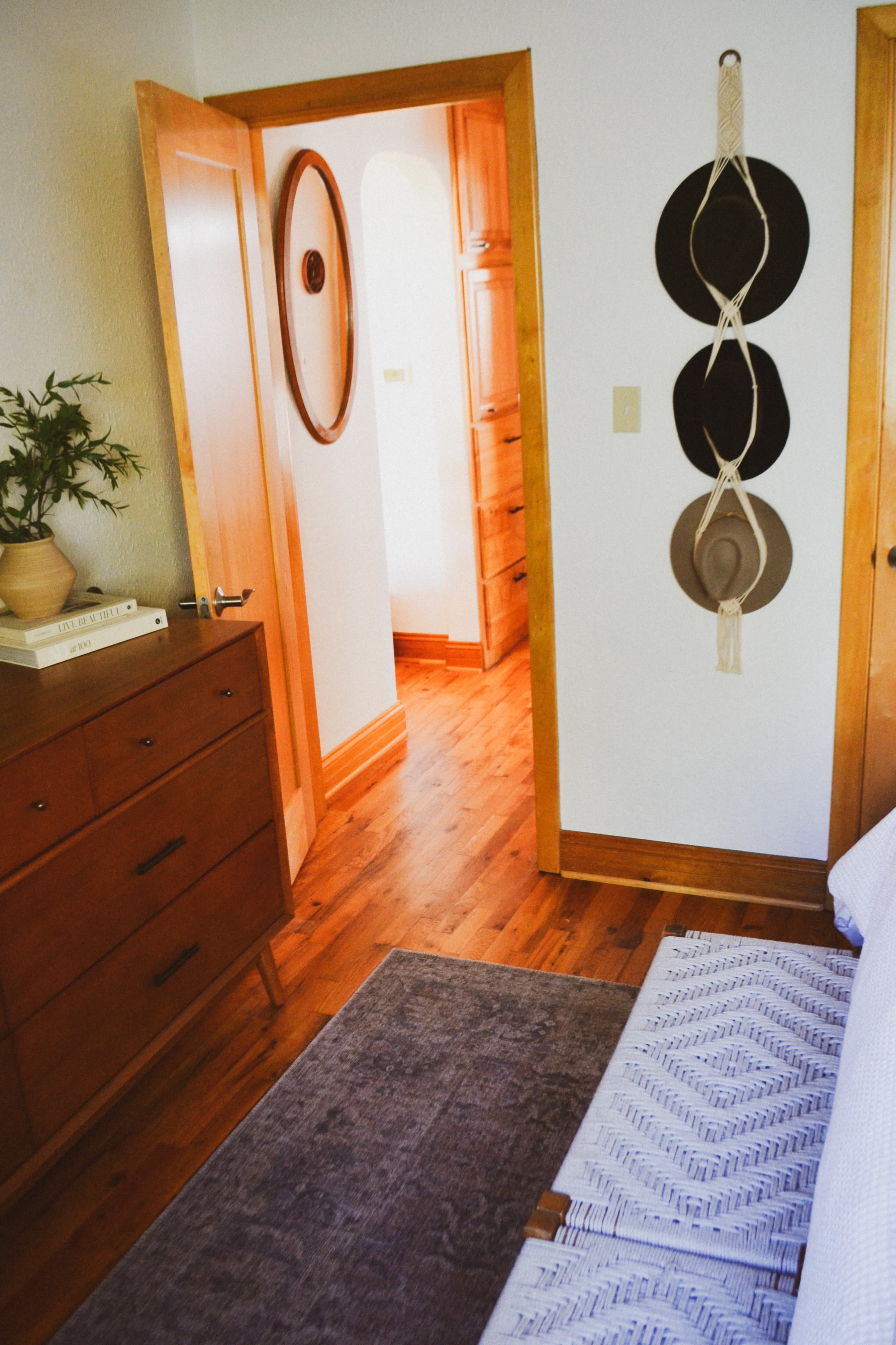 The image shows a cozy bedroom with wooden furniture, a bed with a patterned throw, and a door leading to a hallway.