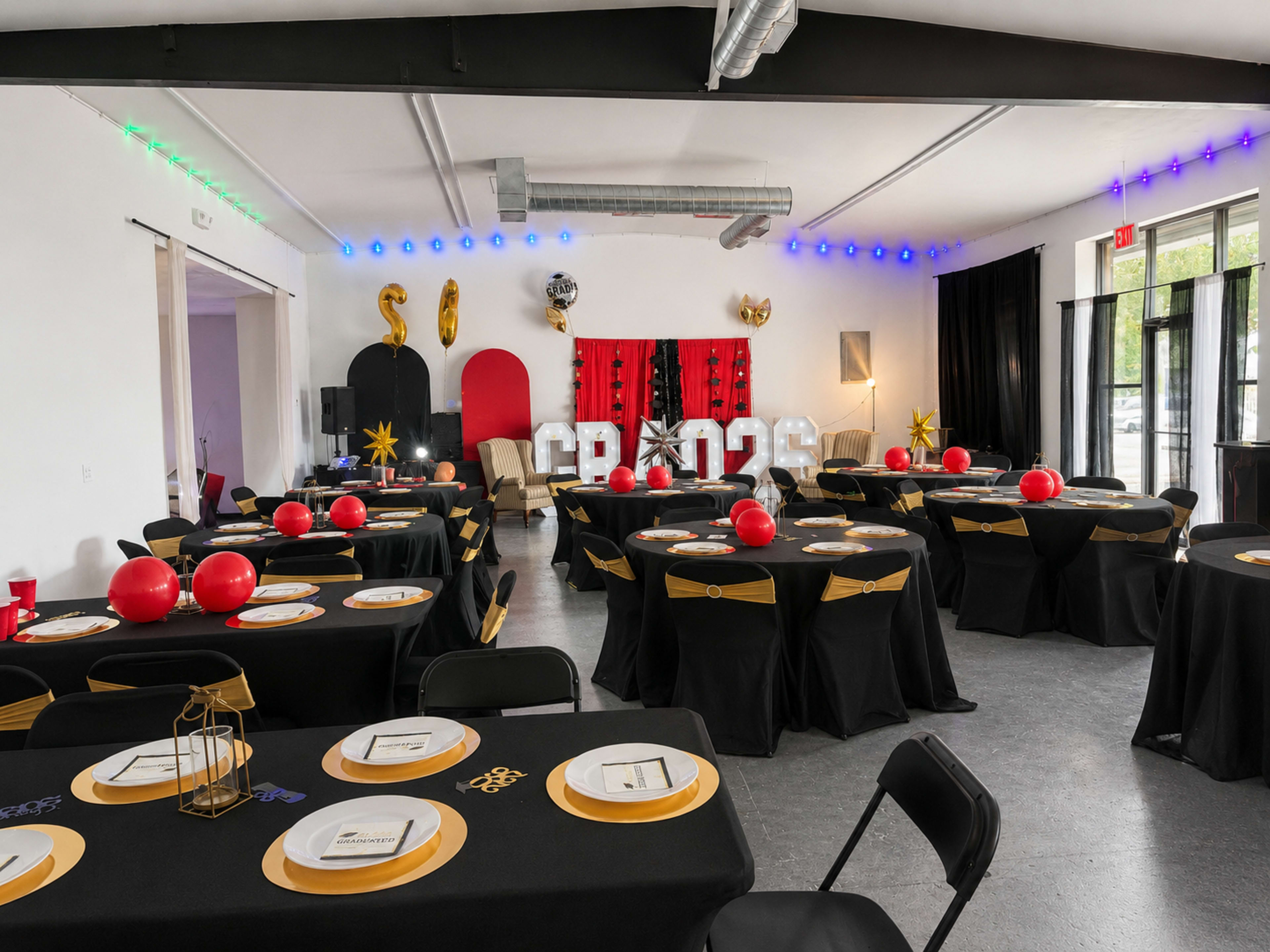 The image shows a decorated indoor event space with tables covered in black tablecloths, red decorations, and large letters spelling "GRAD 2023" on a backdrop.