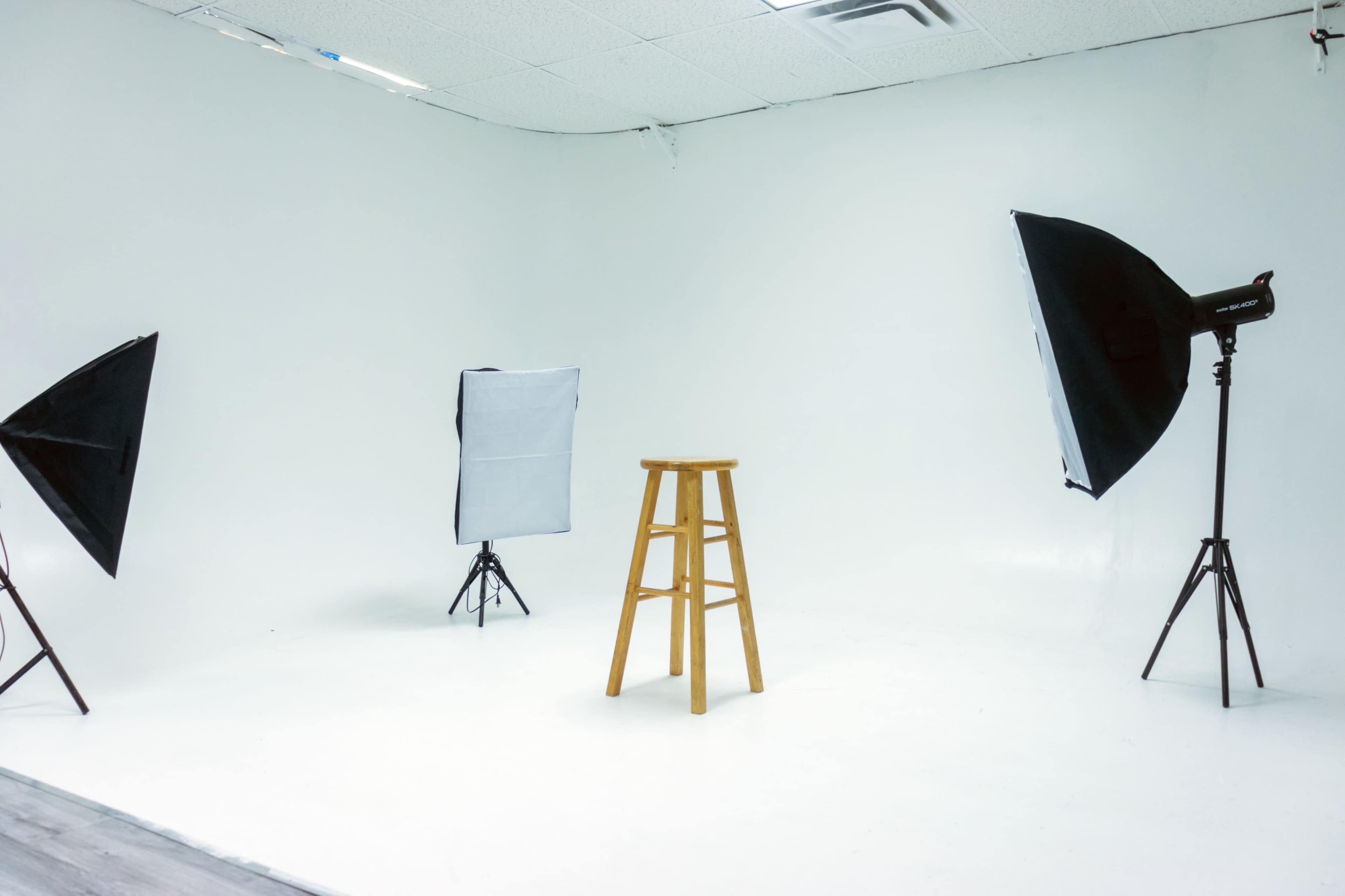 A bare photography studio features a wooden stool in the center, surrounded by three softbox lights on stands.