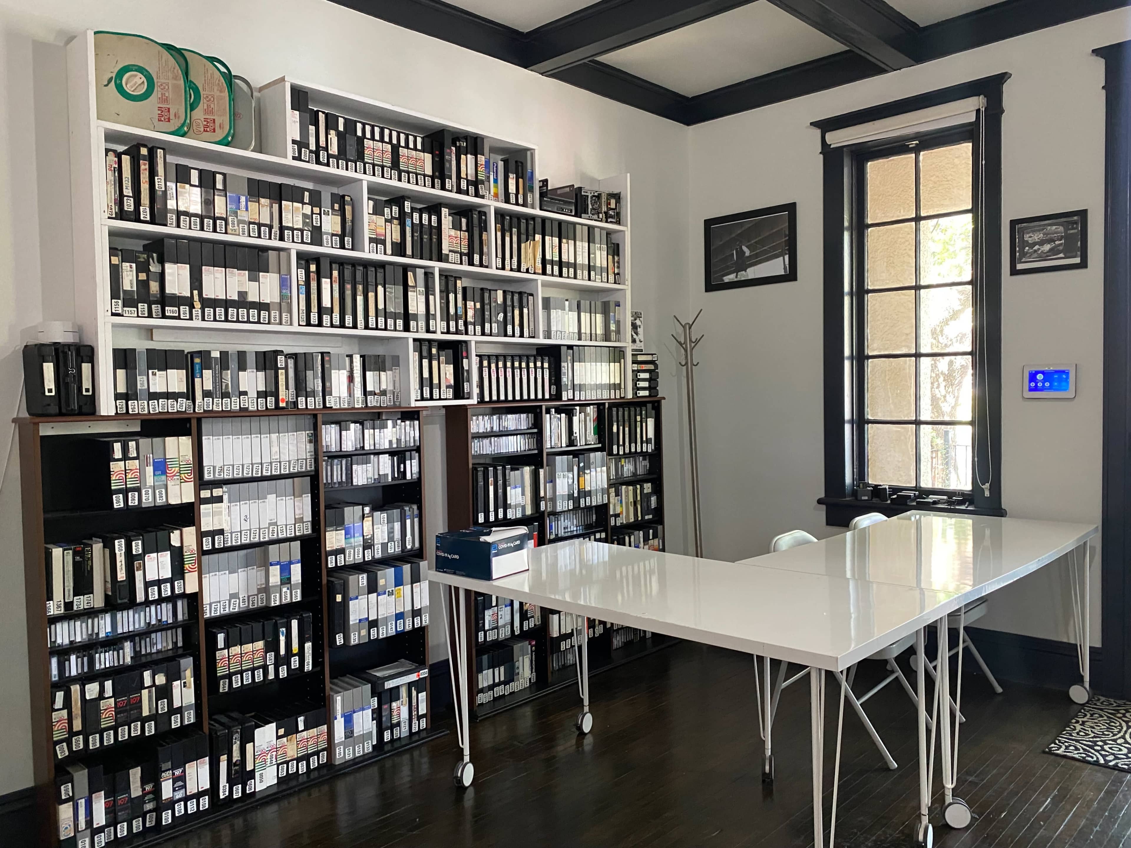 A room with a white table in the center and bookshelves lined with numerous boxes and labeled tape containers along the walls.