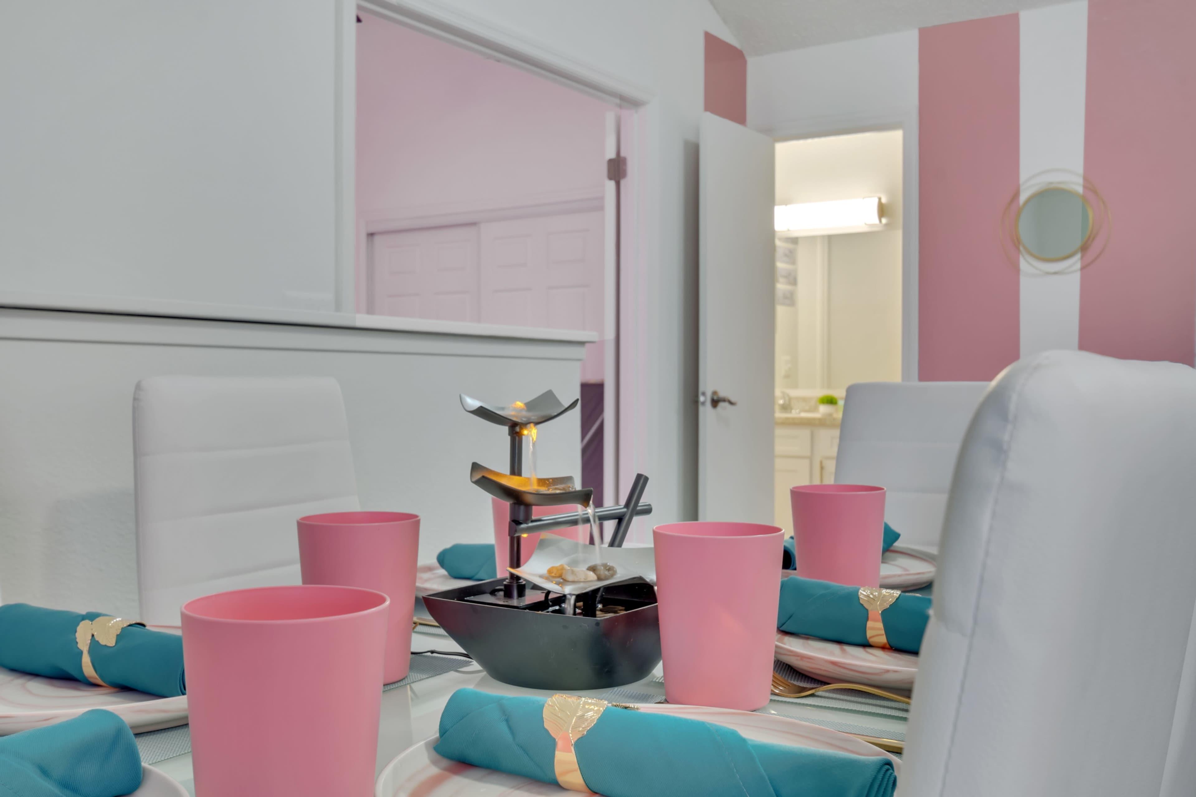 A dining table is set with pink cups and turquoise napkins, featuring a tiered serving stand in the center.