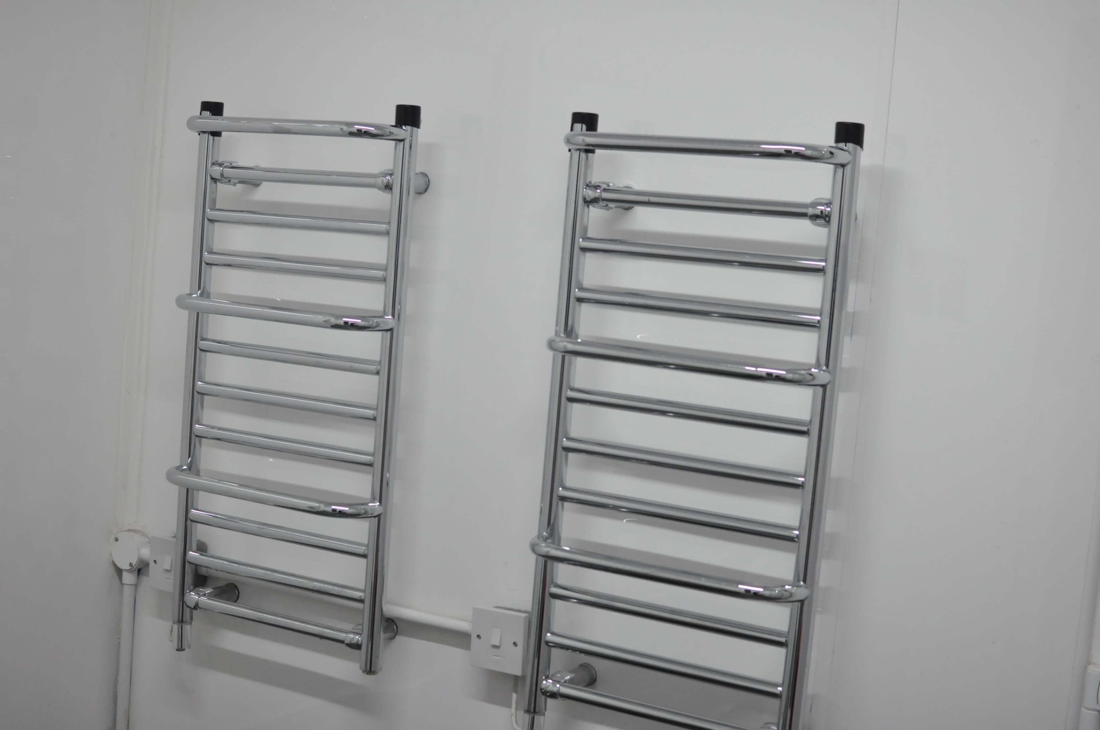 Two chrome towel rails are mounted on a white wall.