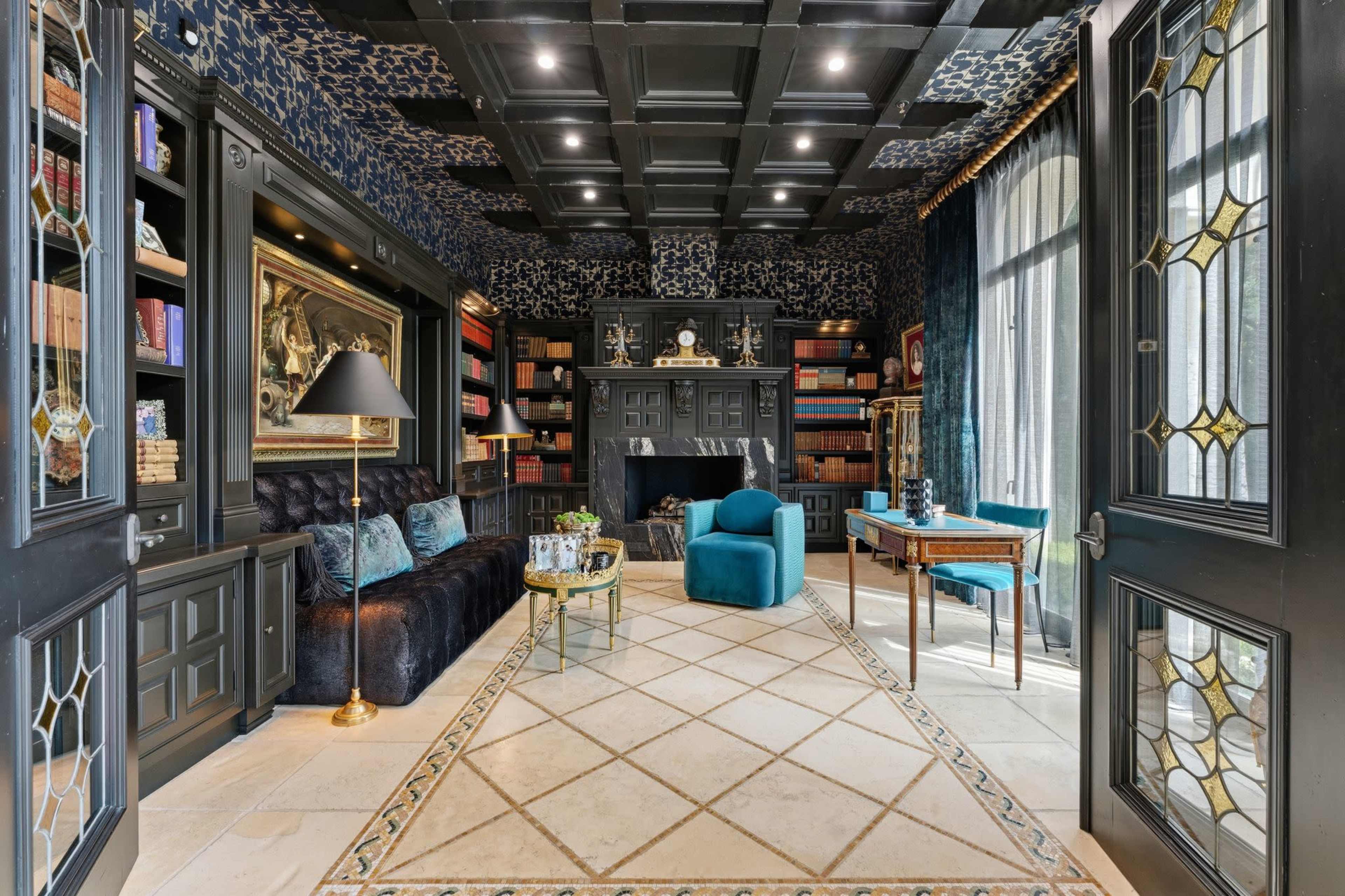 The image depicts a stylish home library featuring a dark color scheme, a velvet couch, shelves filled with books, a fireplace, and elegant furnishings.