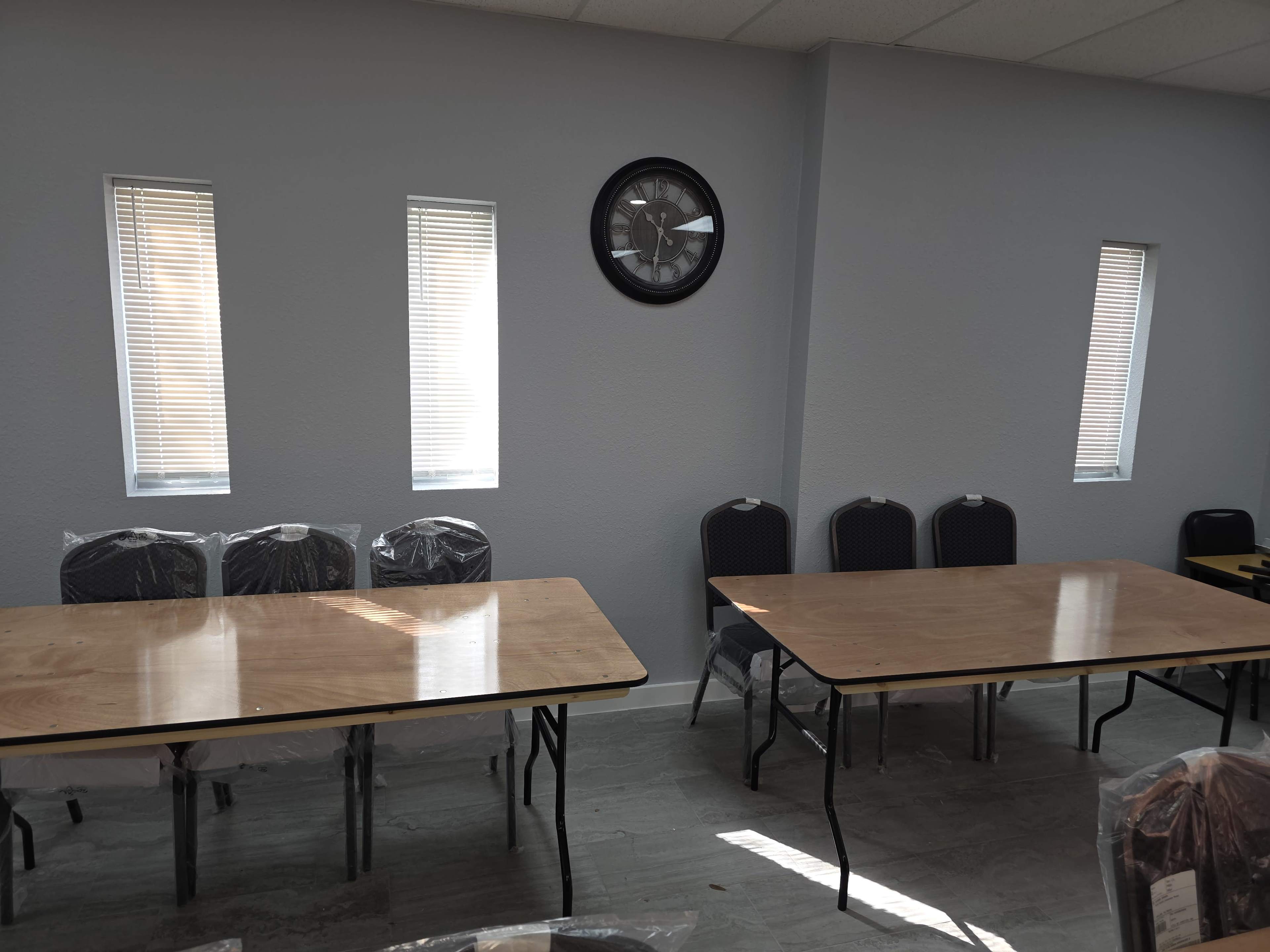 The image shows a room with two tables and several chairs, with light streaming through four narrow windows.