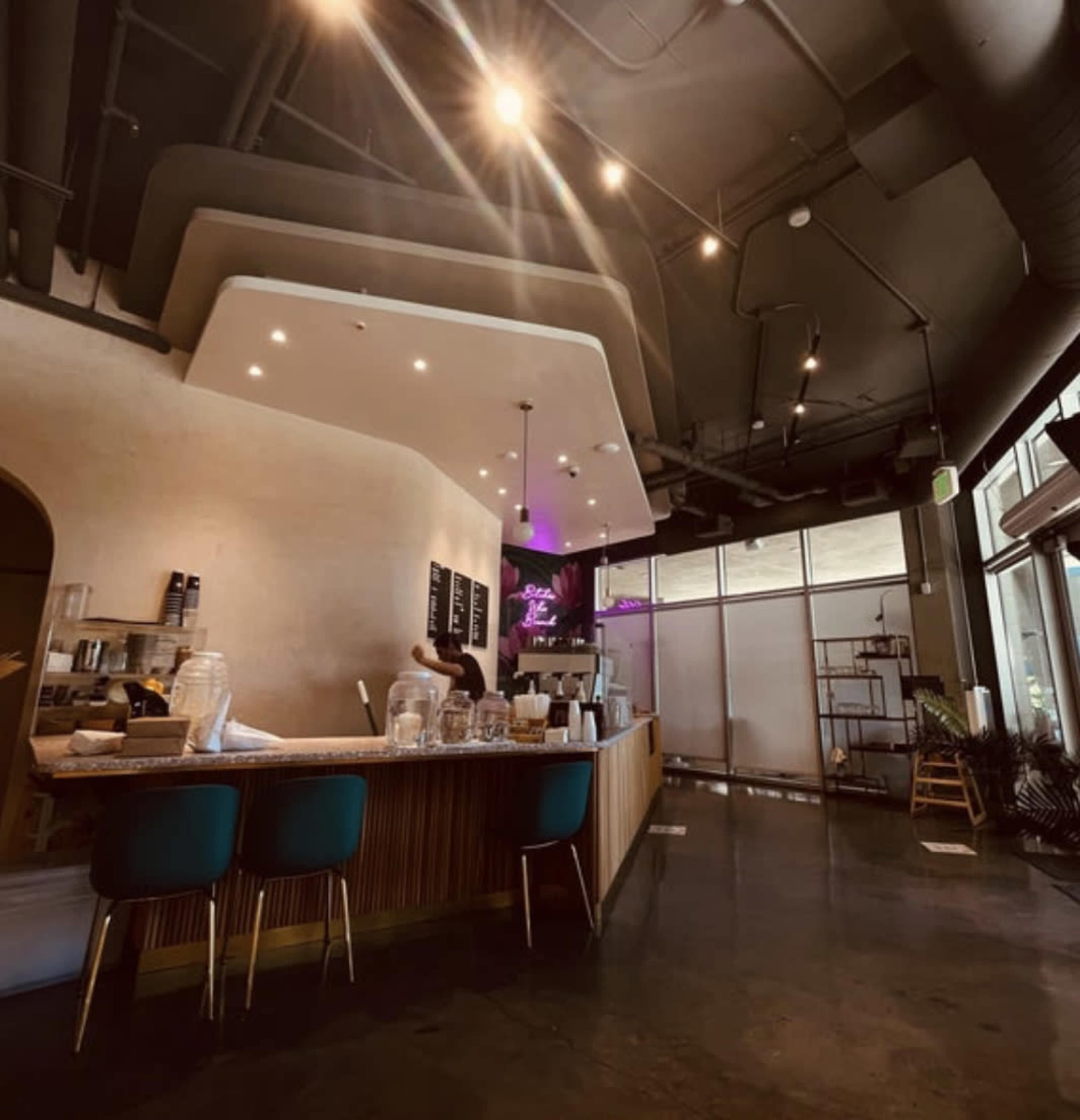 A modern cafe interior with a curved counter, several barstools, and large windows allowing natural light to enter.