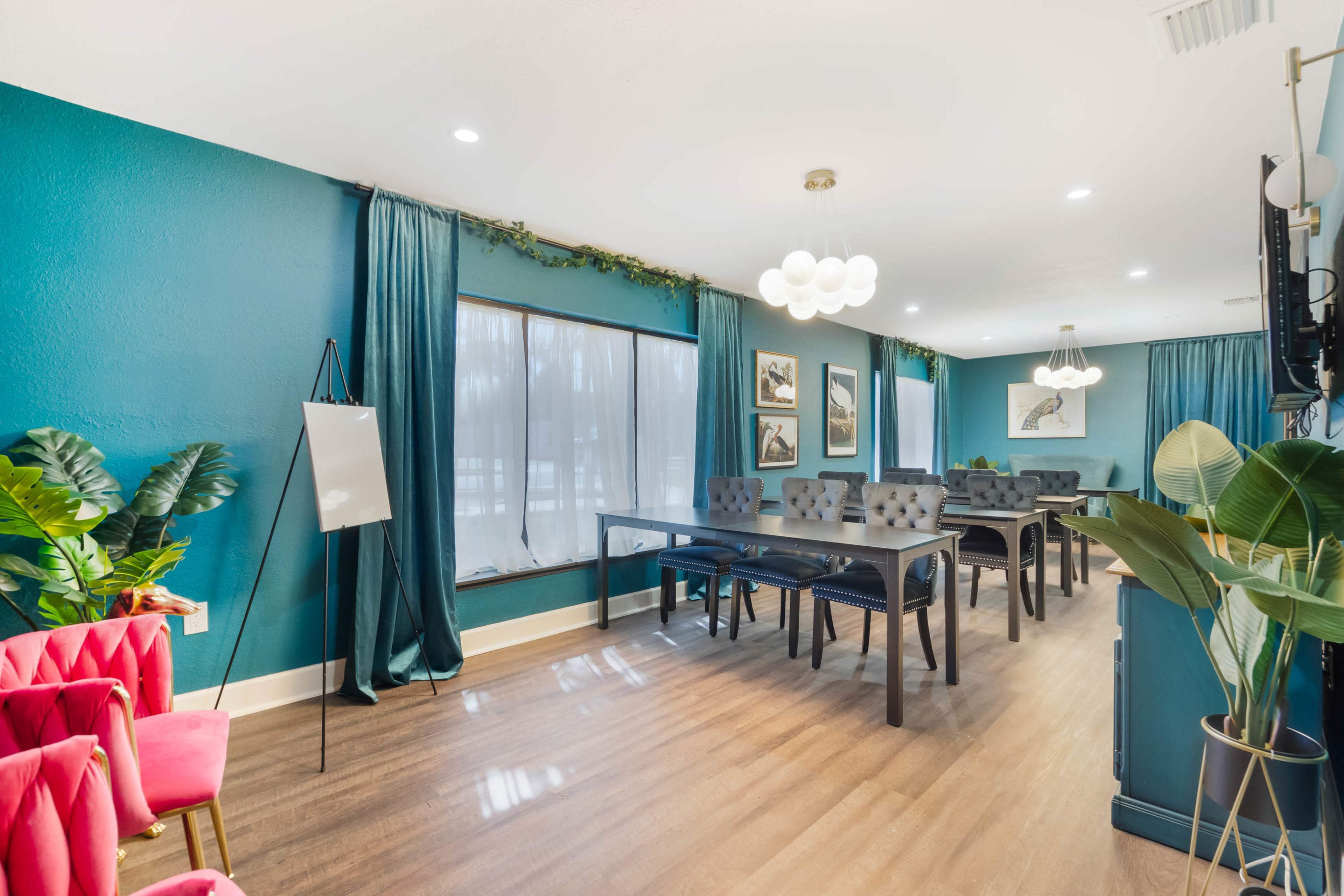 A modern meeting room features dark blue walls, large windows with curtains, and several tables set up for discussions, complemented by plants and stylish decor.