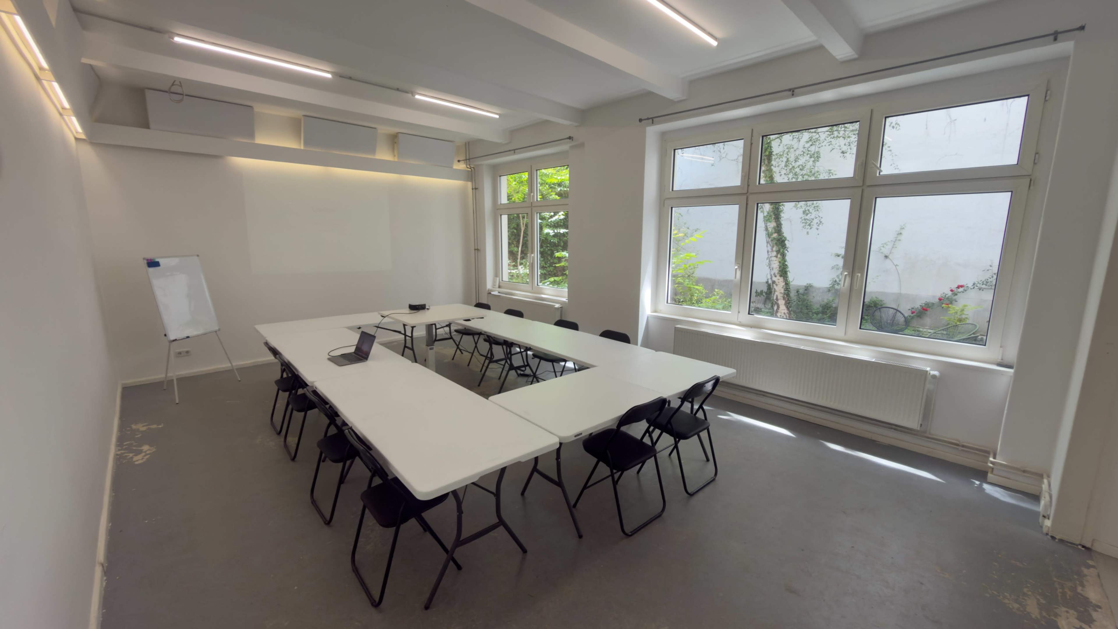 A bright meeting room features a large central table surrounded by black chairs and large windows allowing natural light to enter.