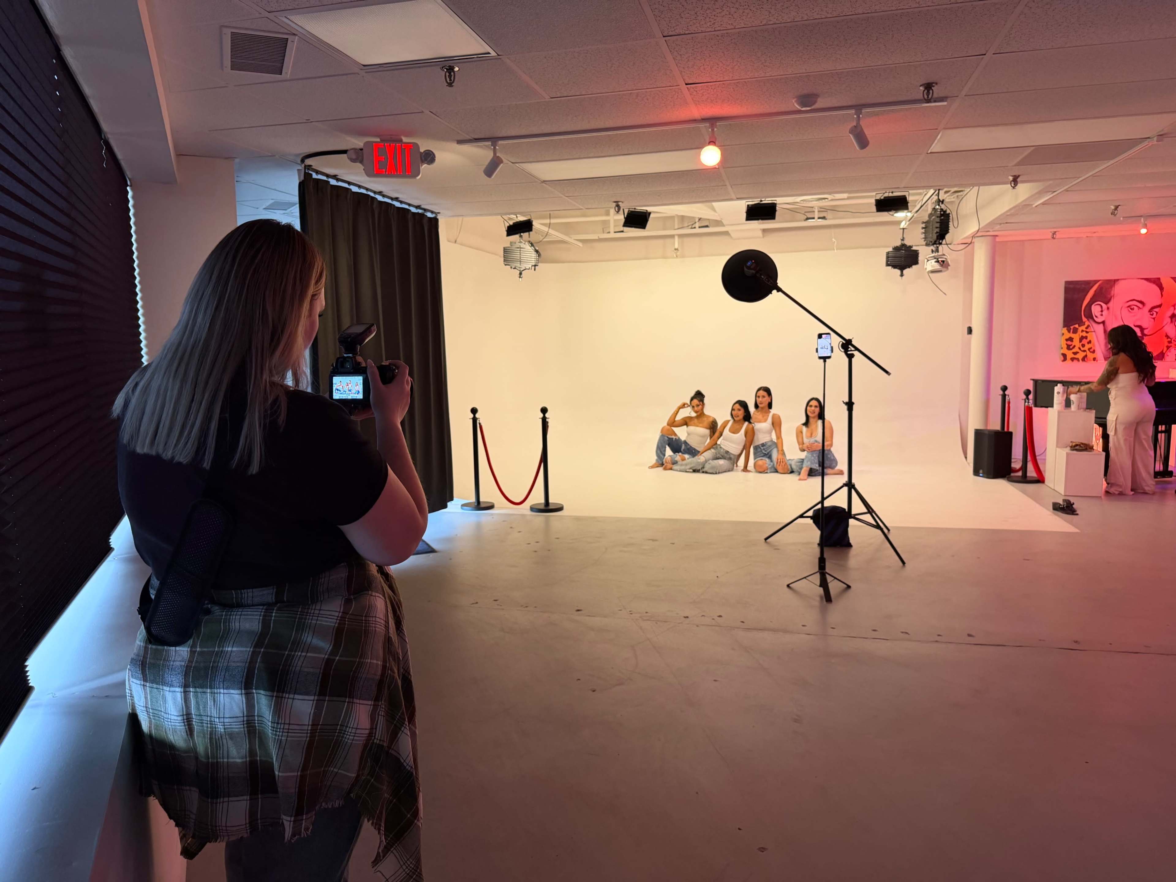 A photographer captures a group of four women posing in a studio setting with lighting equipment and a backdrop.