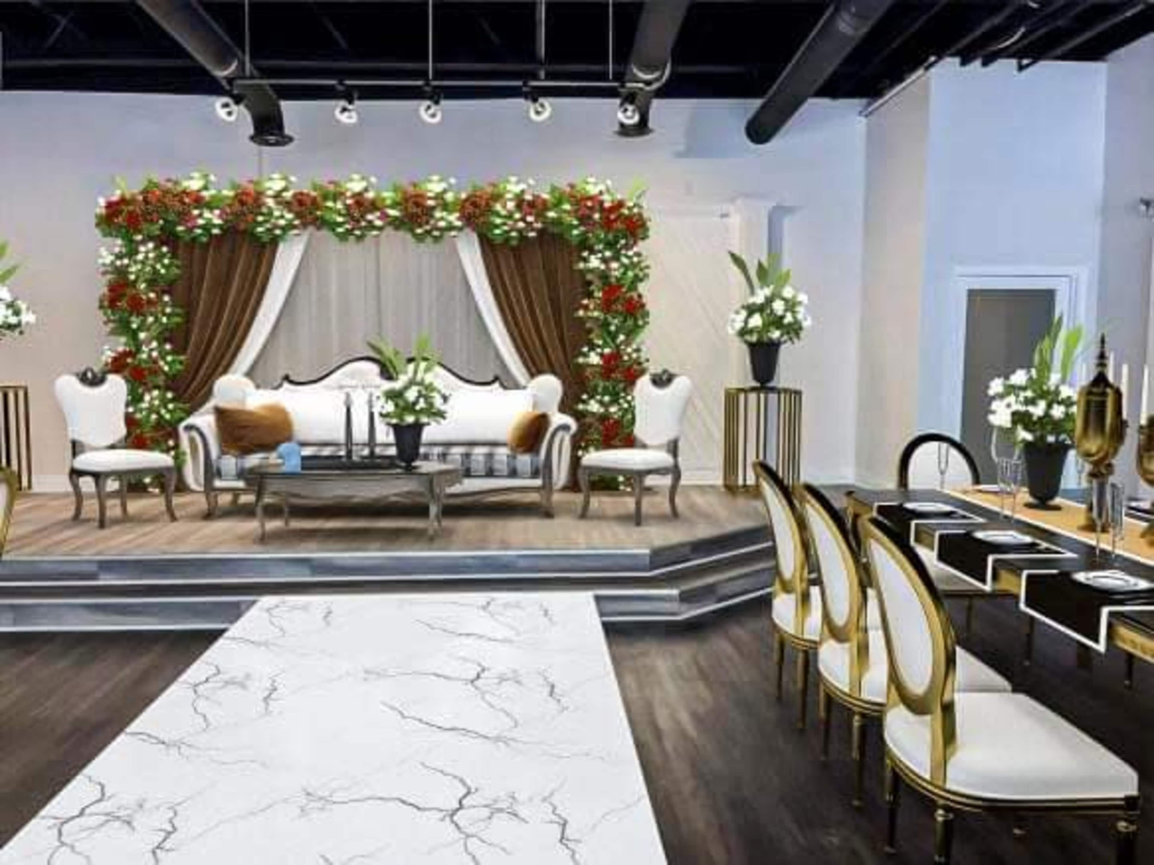 The scene features an elegantly decorated event space with a floral backdrop, a sofa, a coffee table, and a dining area set with chairs and a contrasting table.