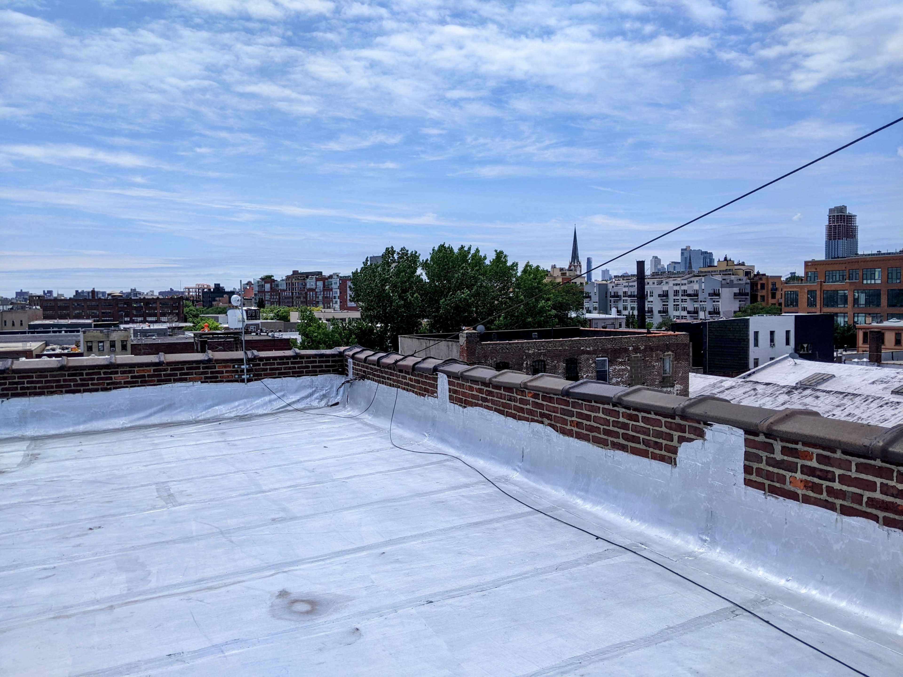 A flat rooftop with a view of urban buildings and a church spire against a partly cloudy sky.