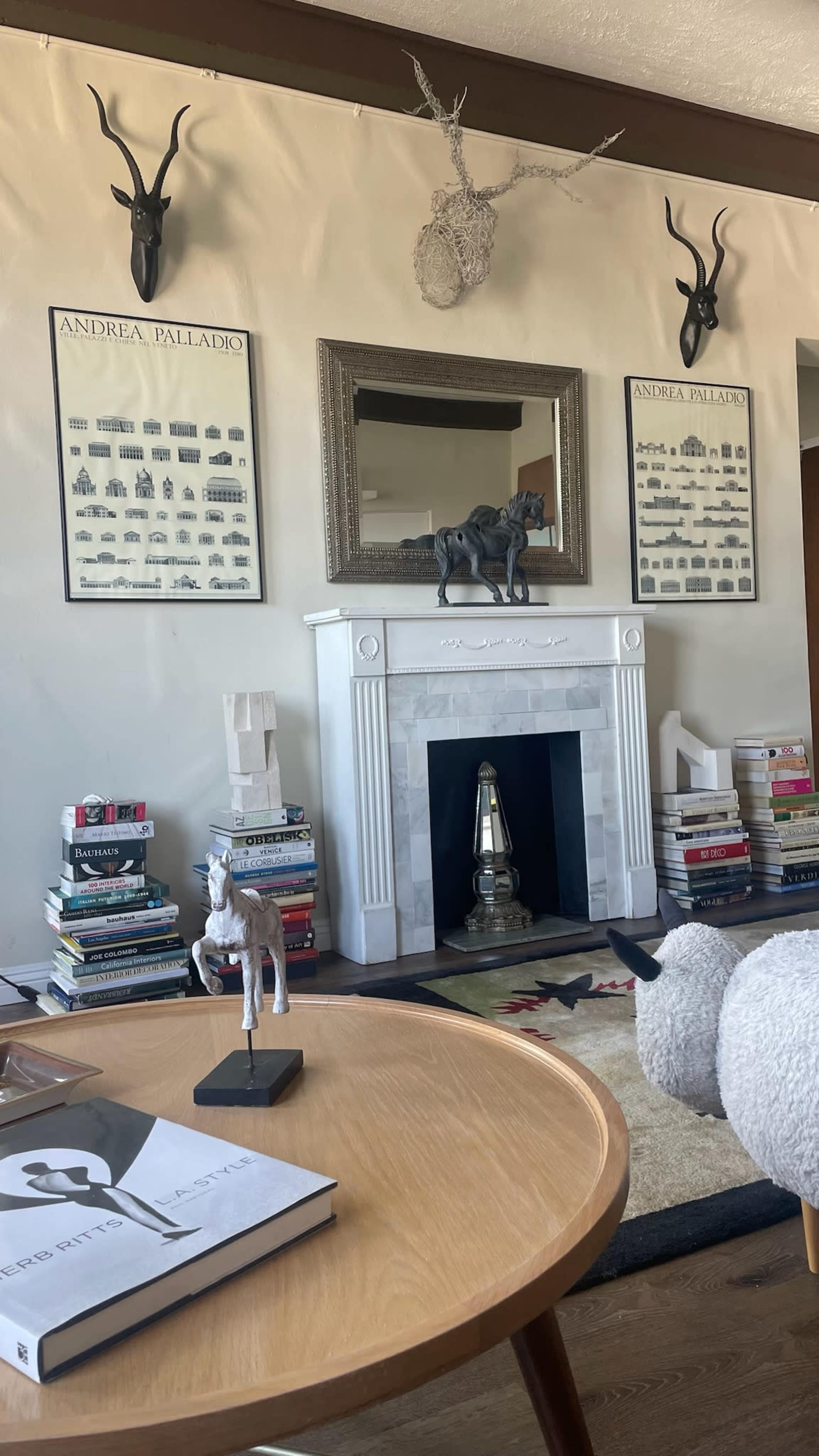 A modern living room features a marble fireplace surrounded by bookshelves stacked with books, decorative animal heads on the walls, and a mirrored display above the mantel.