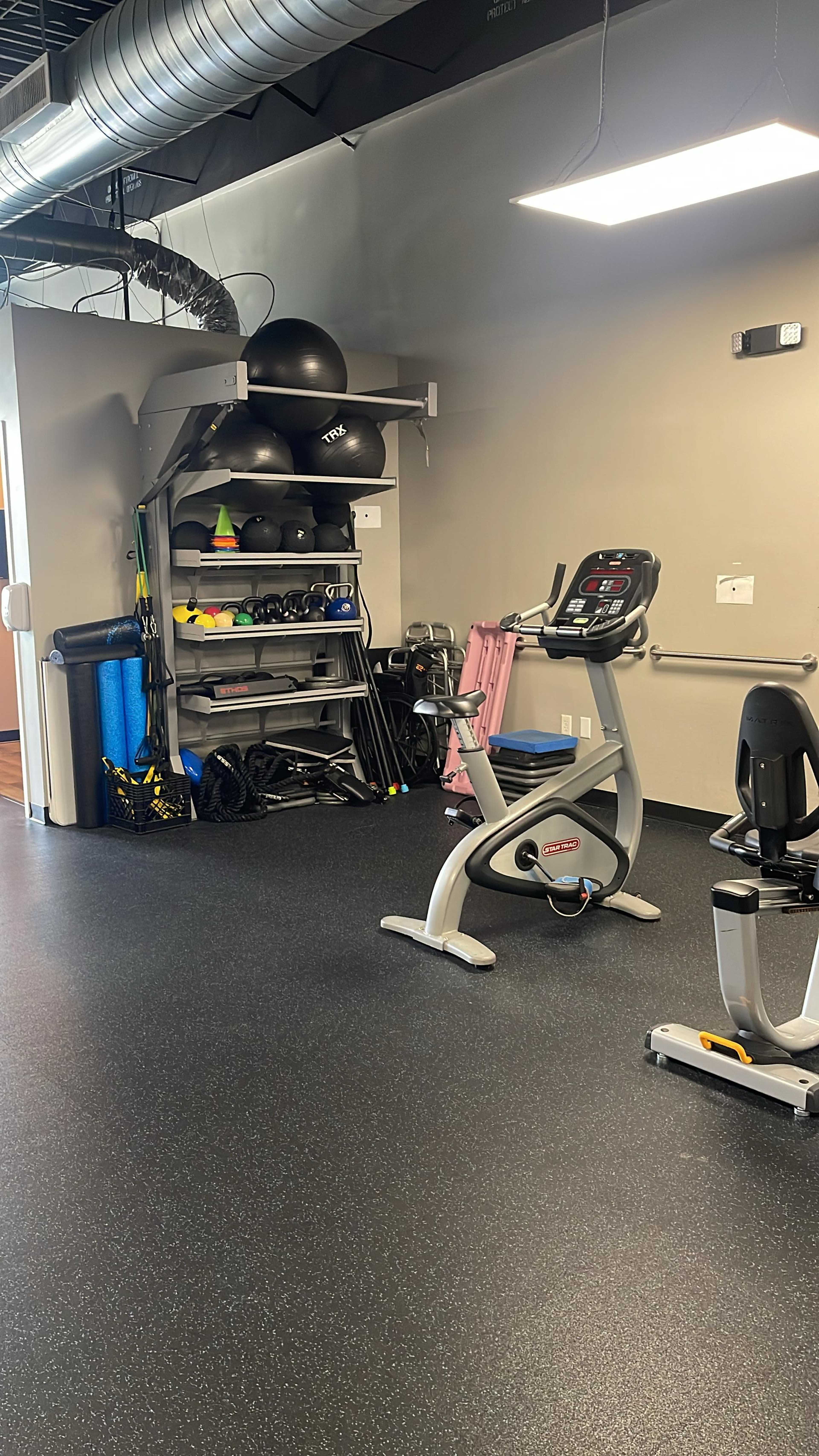 The image shows a fitness area featuring a stationary exercise bike and various gym equipment stored on shelves.
