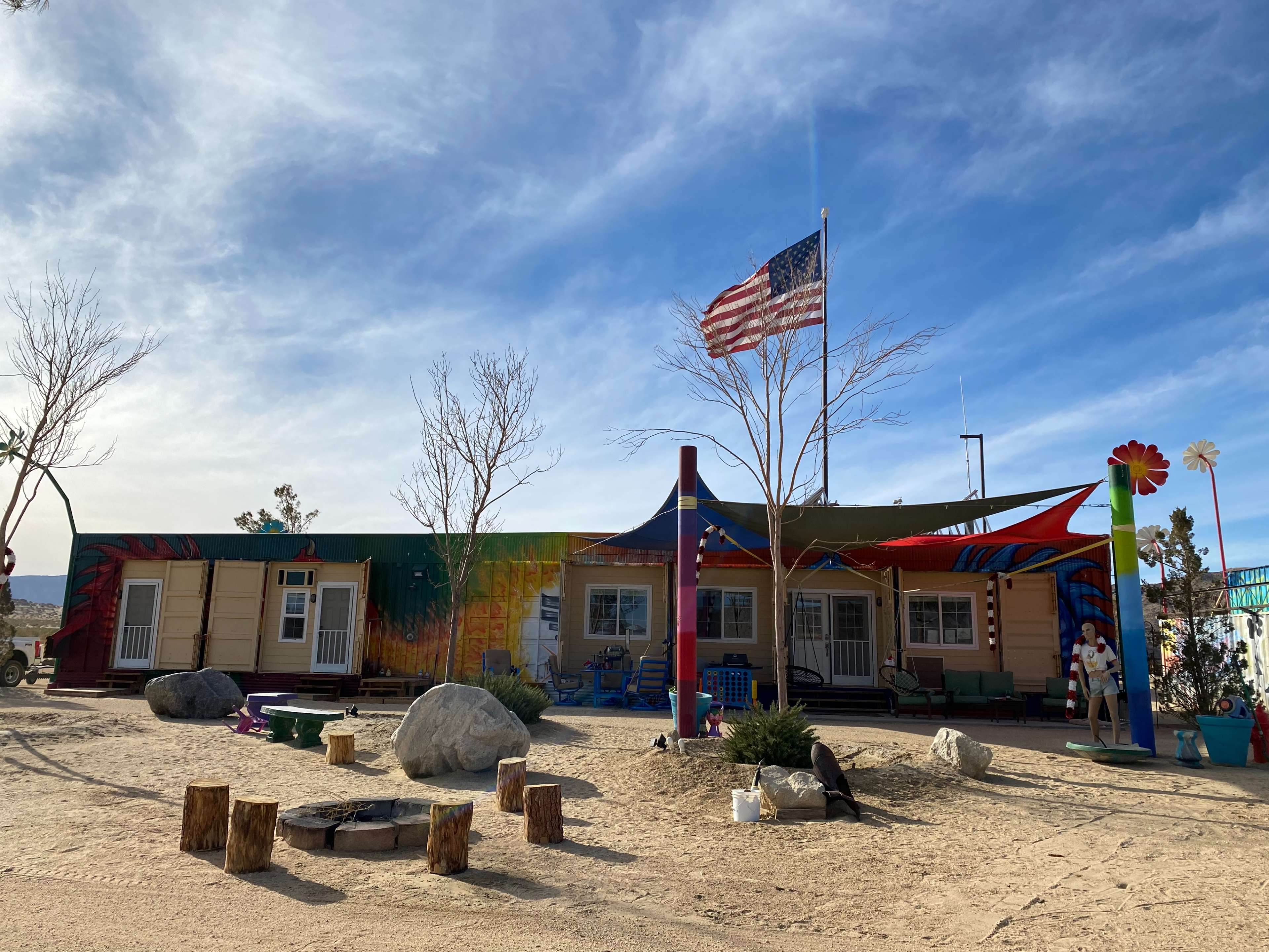 A colorful building with a large American flag in front is surrounded by desert vegetation and decorative elements.