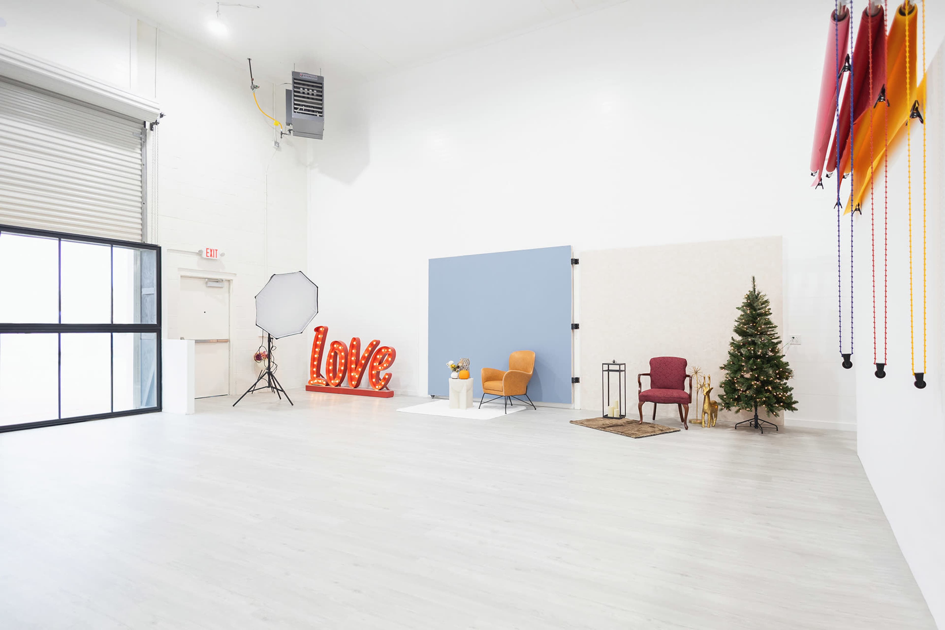 The image shows a spacious, well-lit studio with a decorated area featuring a large "Love" sign, various seating arrangements, and a Christmas tree, alongside colorful backdrops hanging on the wall.