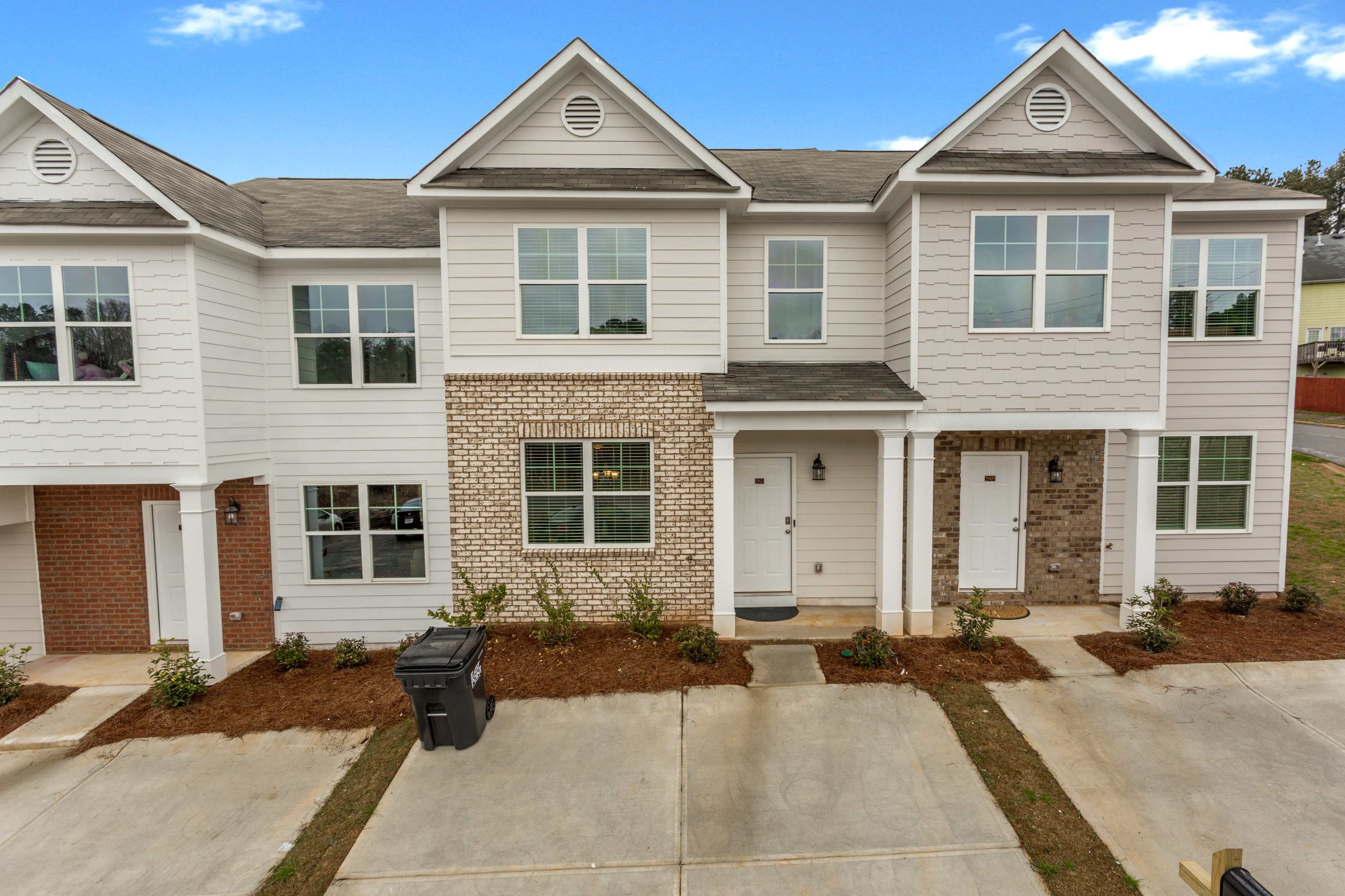 A row of three attached townhouses with varying exterior finishes, featuring brick and siding, and a neatly landscaped front area.