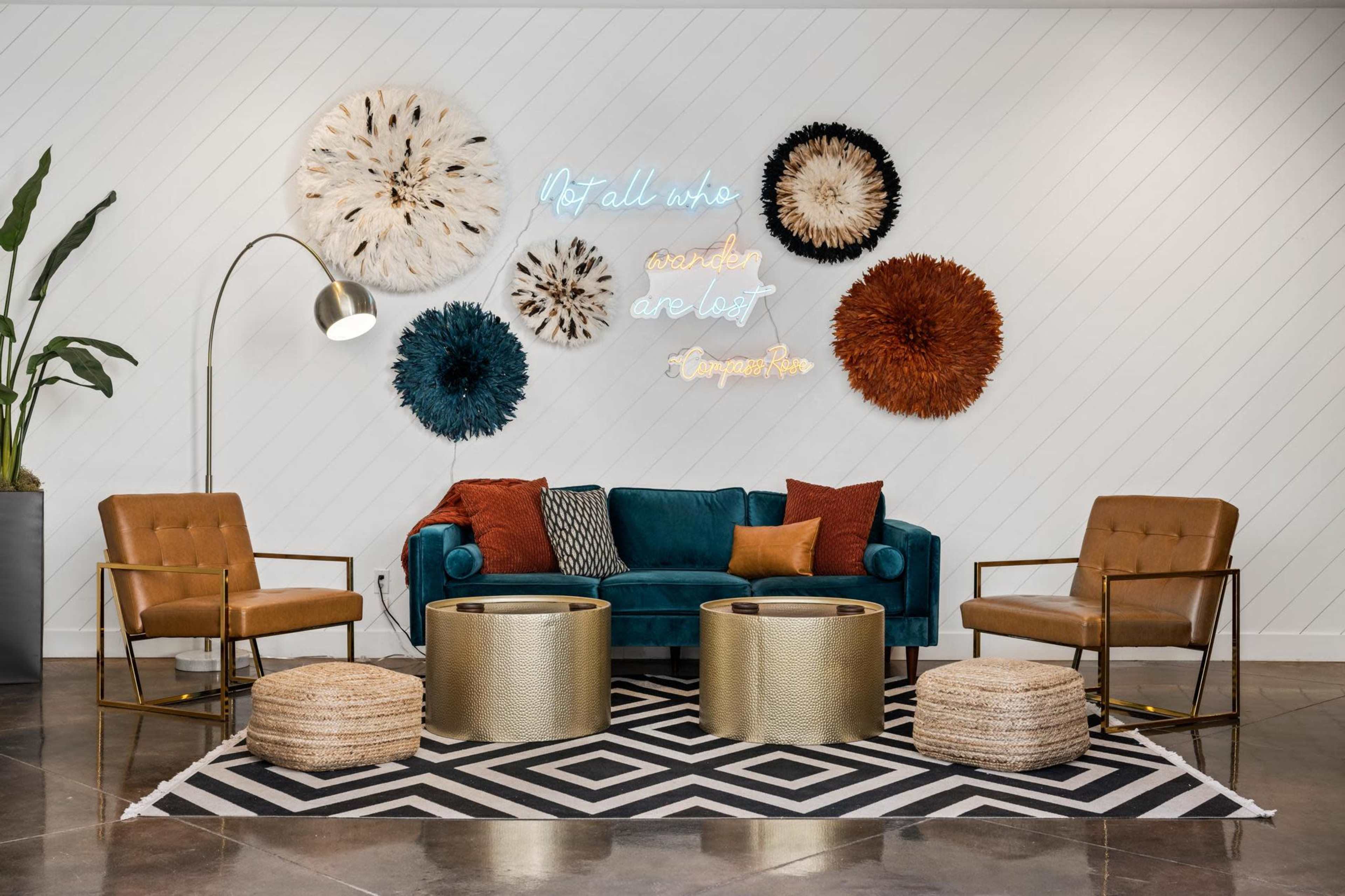 A modern seating area features a teal velvet sofa, gold accent chairs, and decorative wall art, including a neon sign.