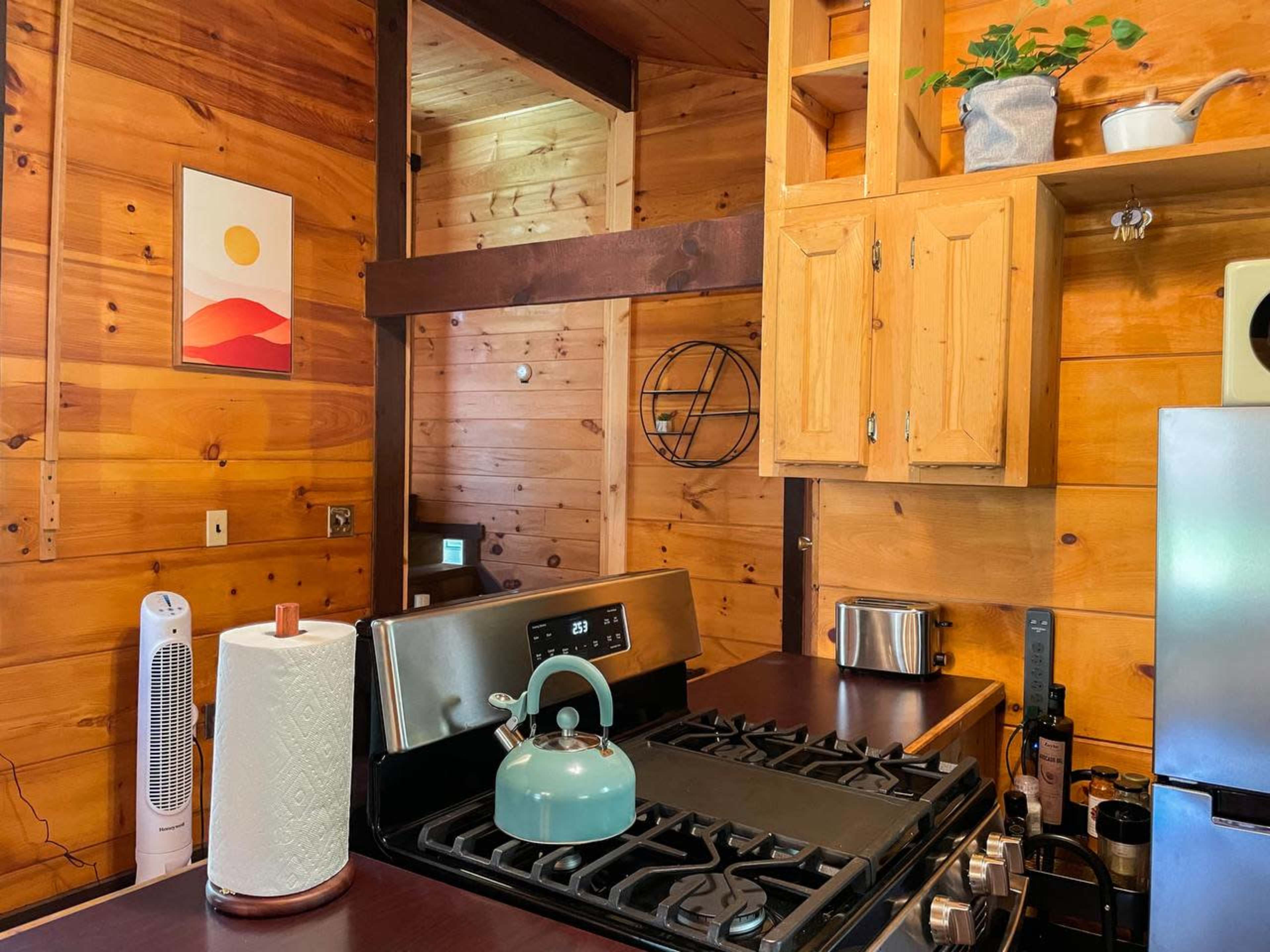 A wooden kitchen with a gas stove, cabinets, and a green kettle on the countertop.