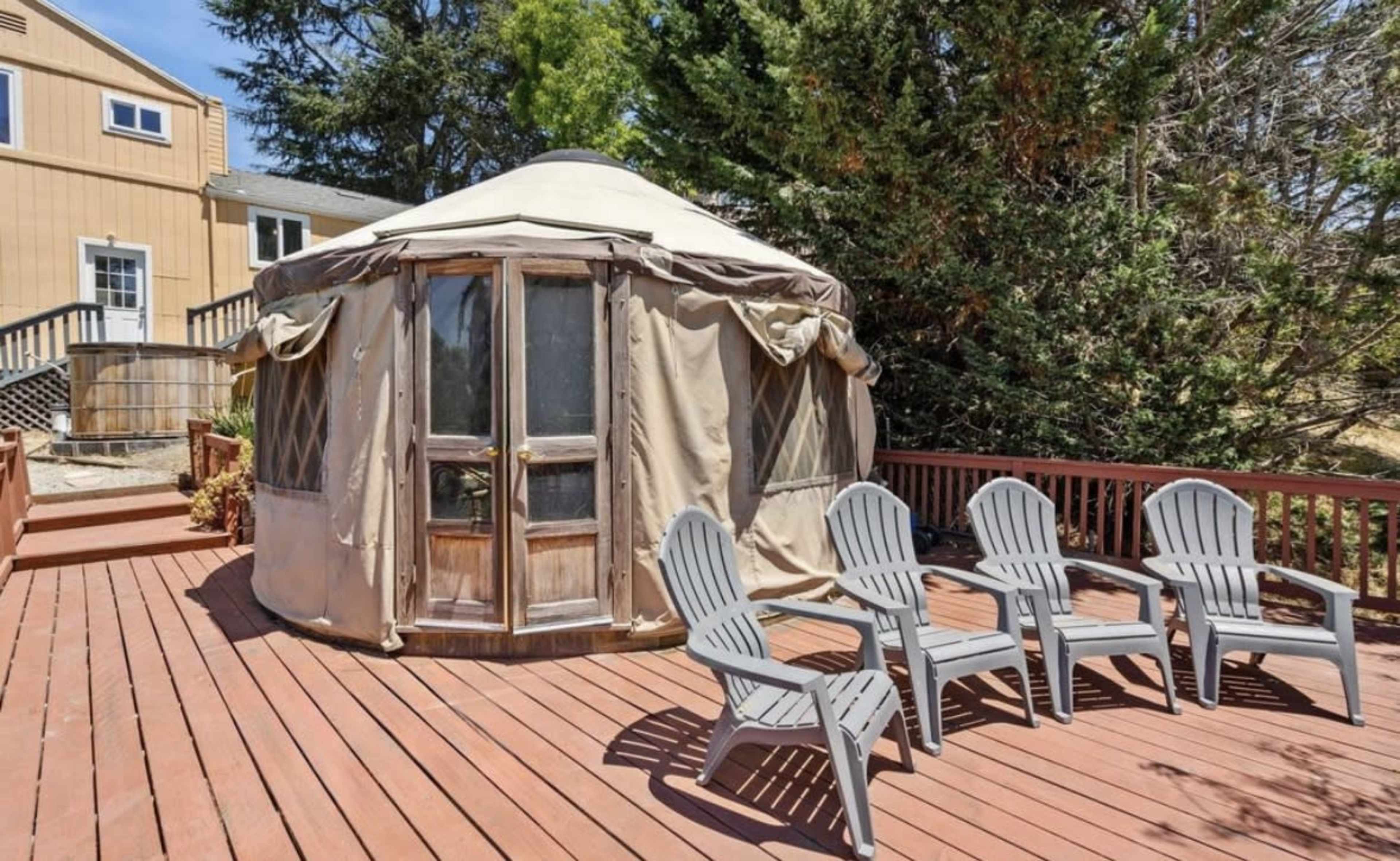 A wooden deck features a round, canvas-covered yurt surrounded by several gray outdoor chairs.
