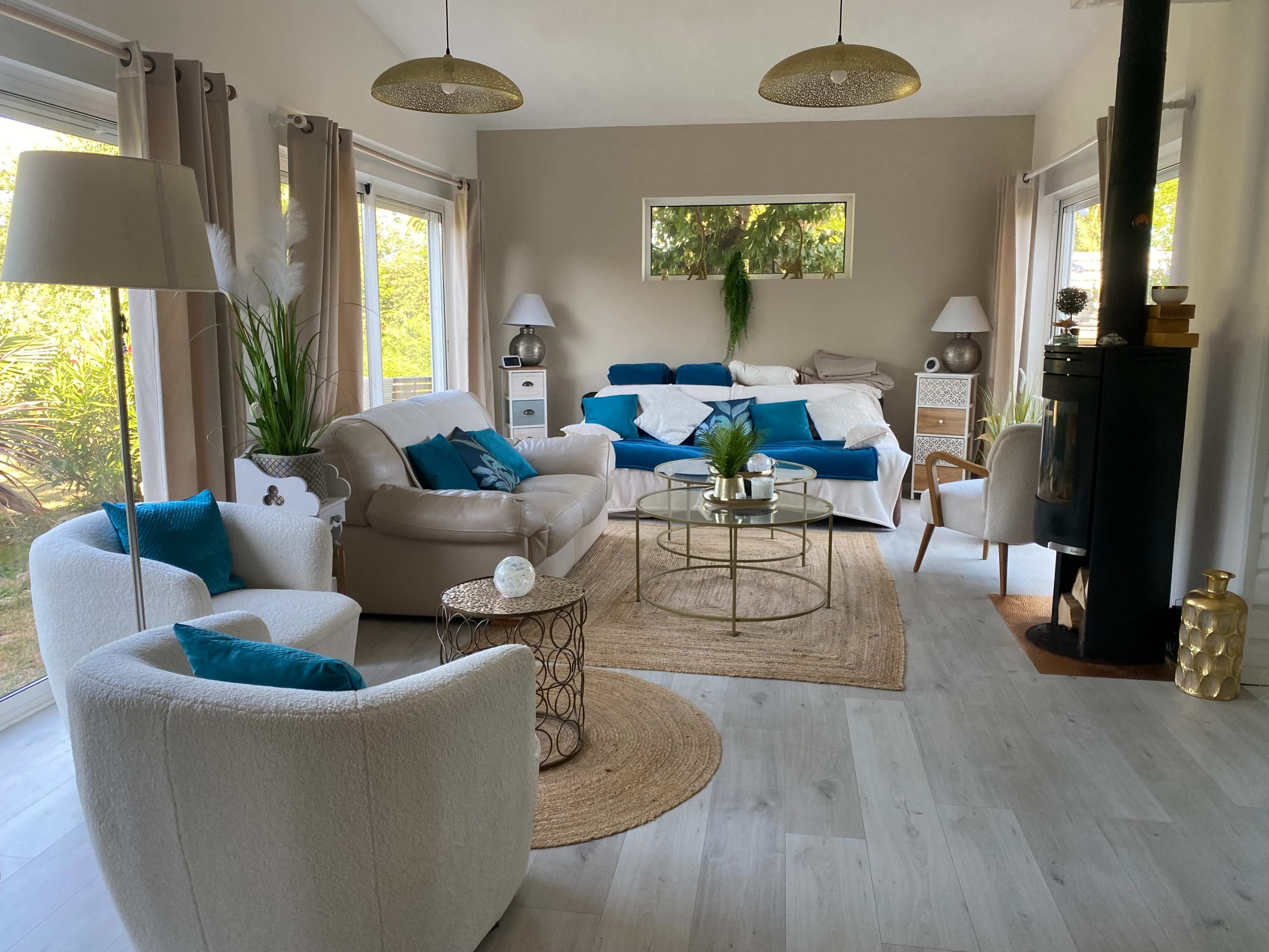 The living room features a light-colored sofa, a round coffee table, and various plants, with large windows letting in natural light.