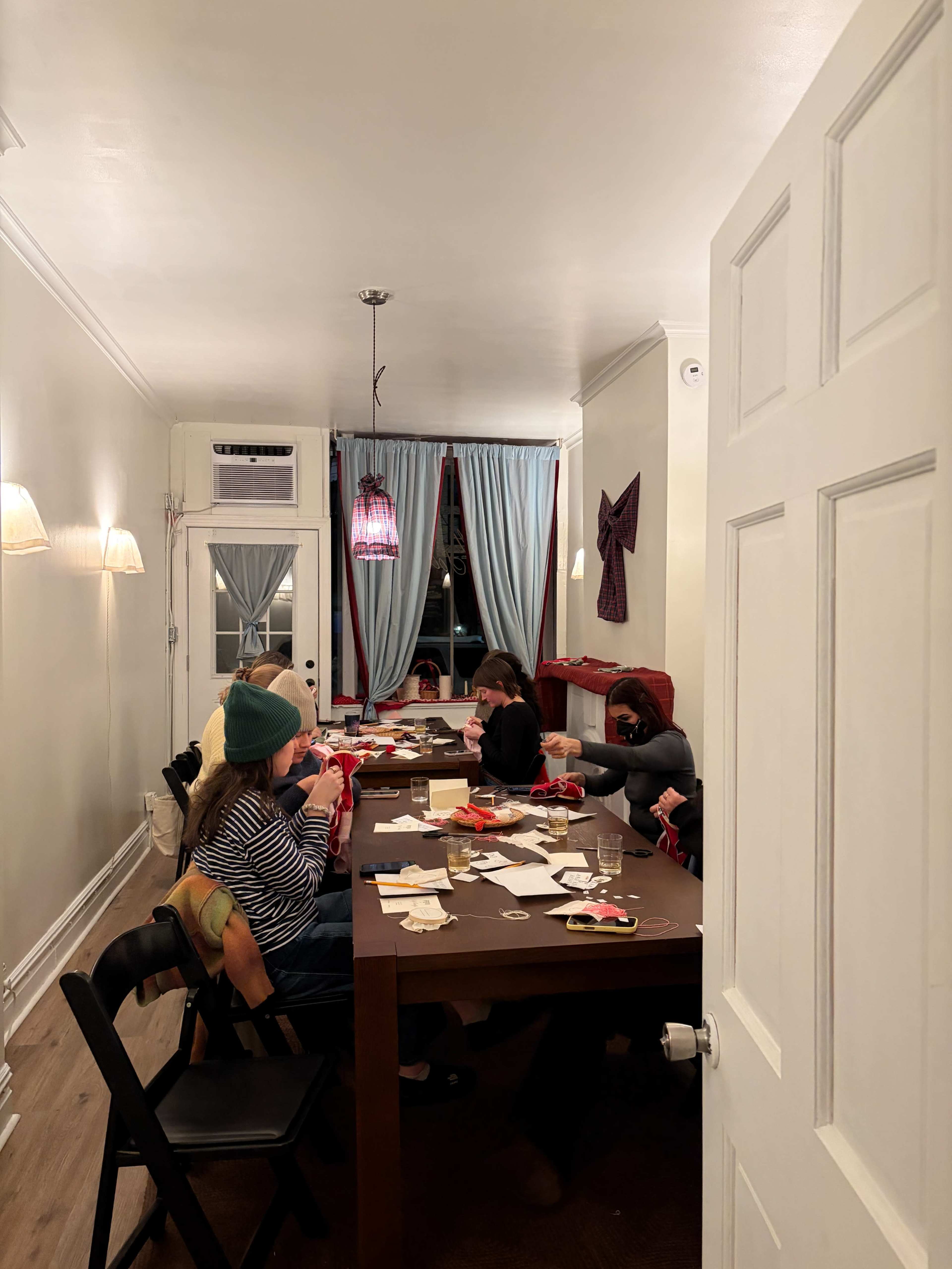 A group of people sits around a long table in a well-lit room, engaged in an activity with various materials scattered on the surface.